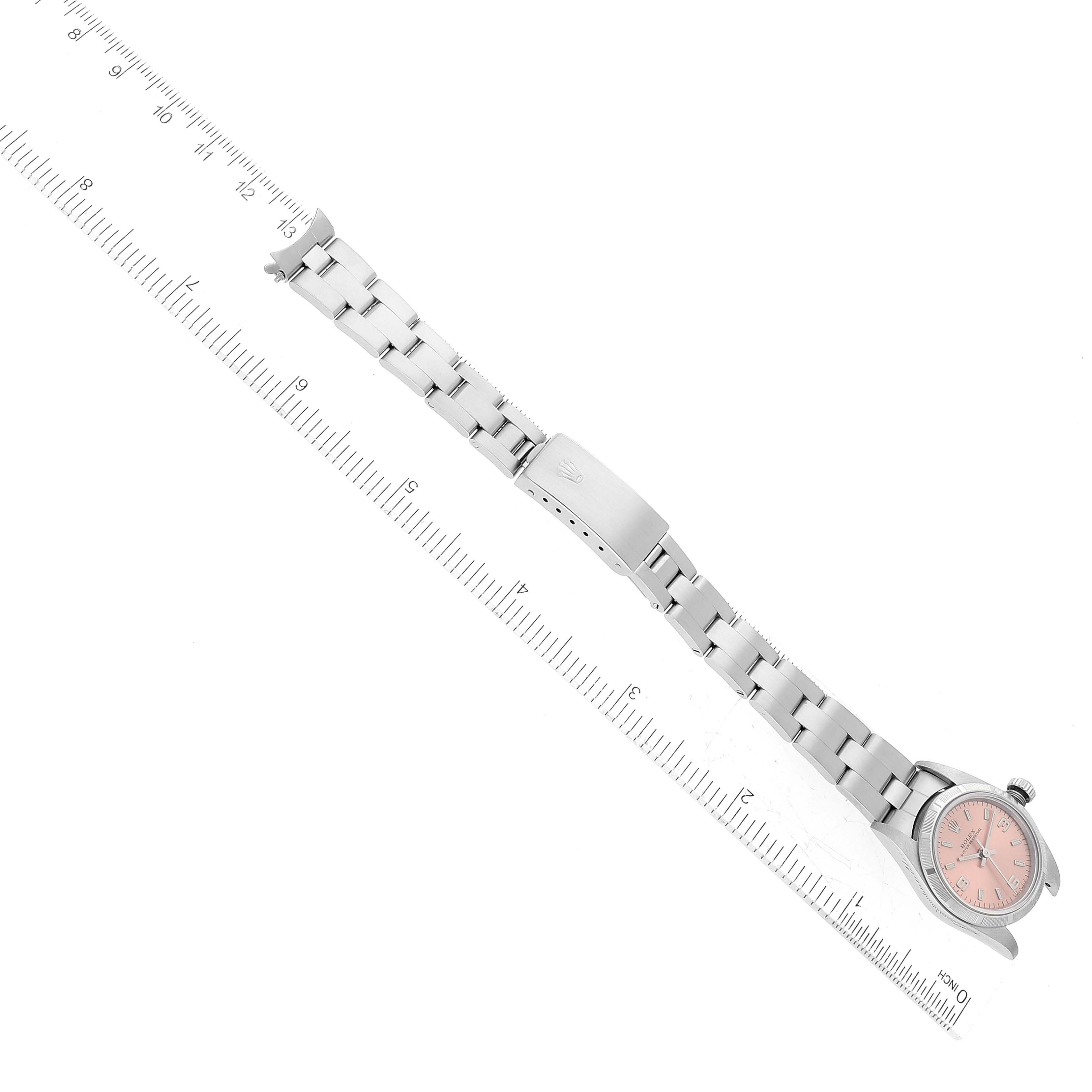 The image shows a Rolex Oyster Perpetual 76030 Women
s Stainless Steel Pink Dial 76030 Women
s Stainless Steel Pink Dial watch laid flat with its pink dial, bracelet, and clasp partially open, alongside a measurement ruler.