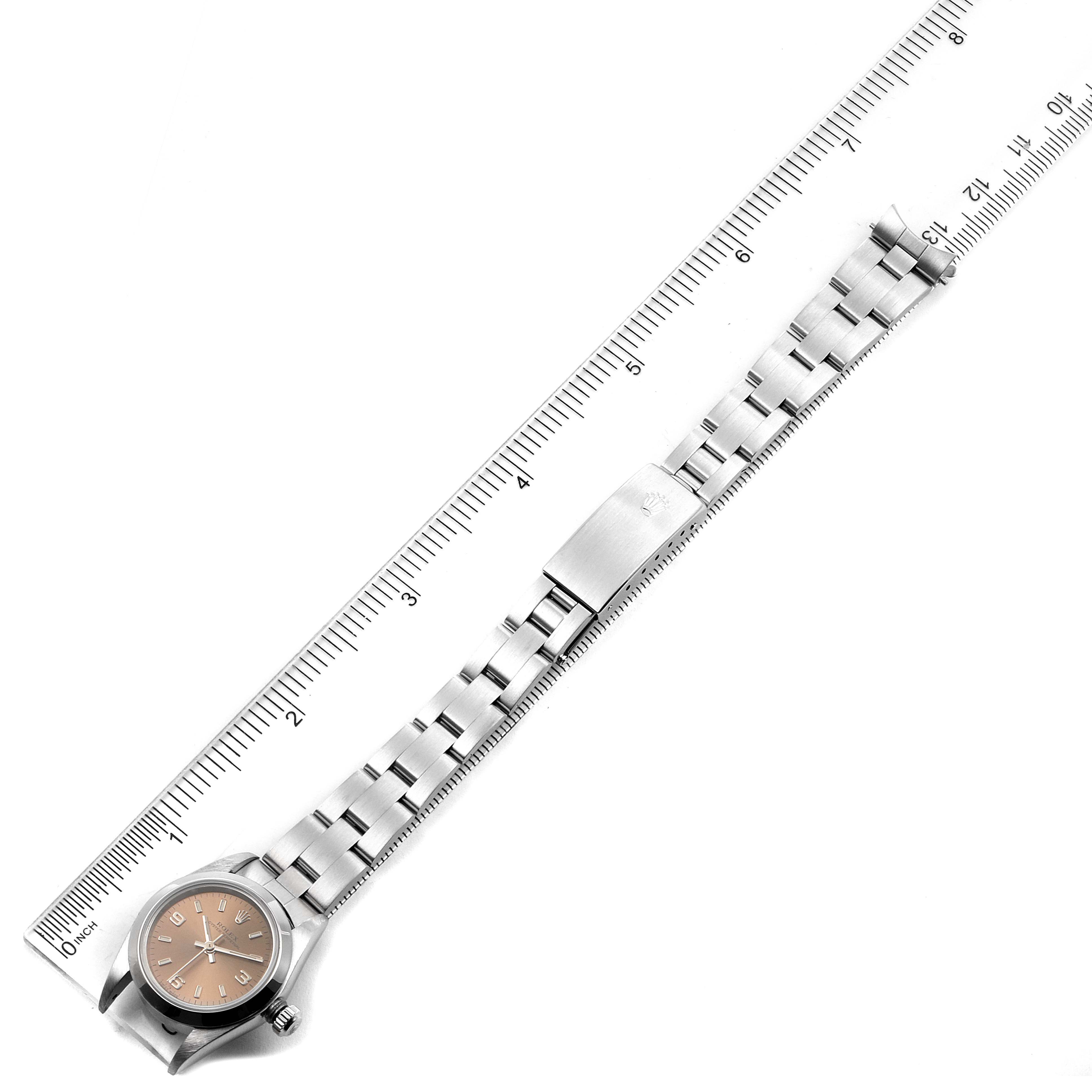This image shows the top view of a Rolex Oyster Perpetual 76080 Women's Stainless Steel Pink Dial 76080 Women's Stainless Steel Pink Dial watch, including its dial, metal bracelet, and clasp next to a ruler.