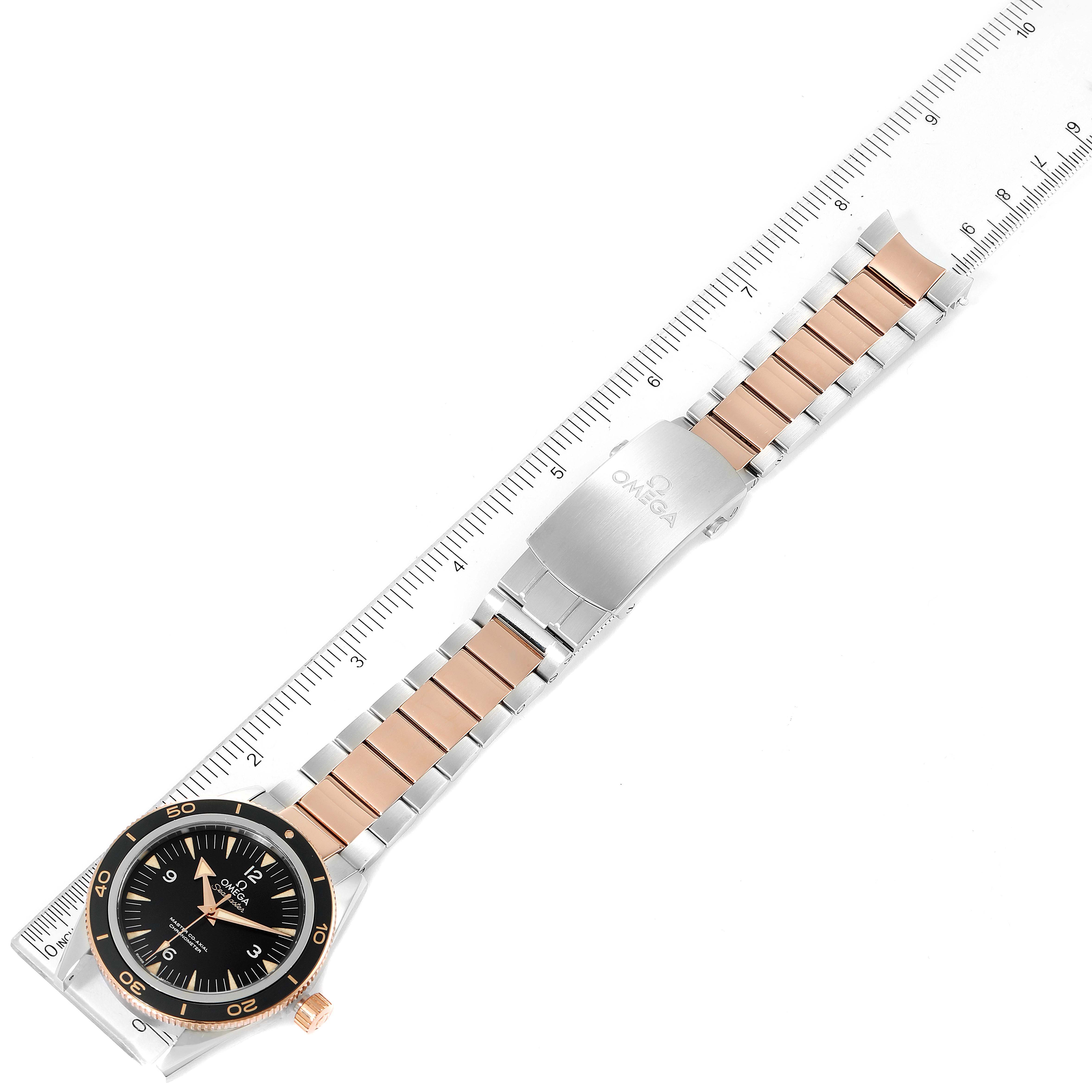 The image displays an Omega Seamaster 233.20.41.21.01.001 Men's Steel and Gold (two tone) Black Dial 233.20.41.21.01.001 Men's Steel and Gold (two tone) Black Dial watch at a top-down angle, showing the face, bezel, strap, and clasp, alongside a ruler for scale.