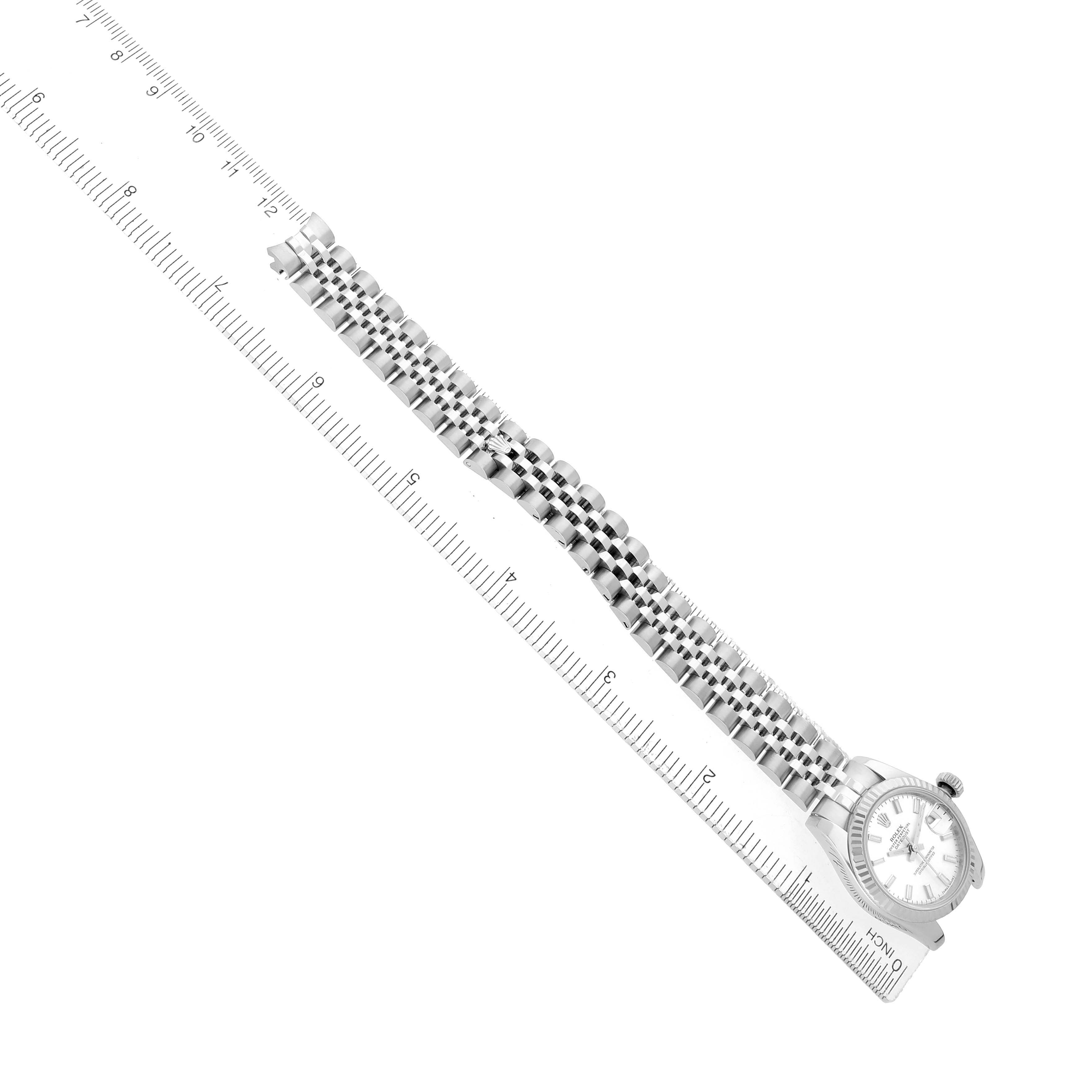The Rolex Datejust 179174 Women
s Stainless Steel Silver Dial watch is shown at an oblique angle, displaying the dial, bezel, bracelet, and a ruler for scale.