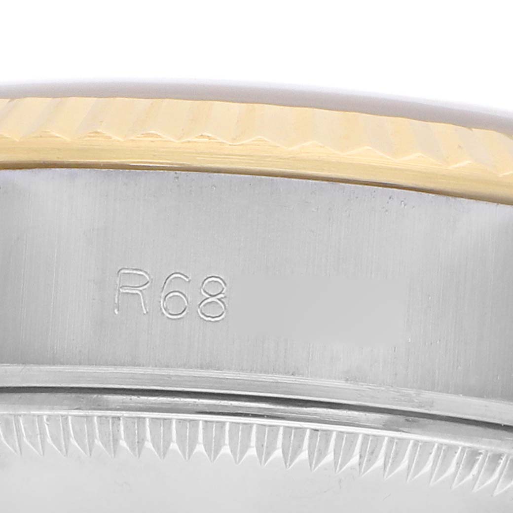 The image shows a close-up of the Rolex Datejust 69173 Women
s Steel and Gold (two tone) Silver Dial watch
s case edge and fluted bezel with partial engraving.