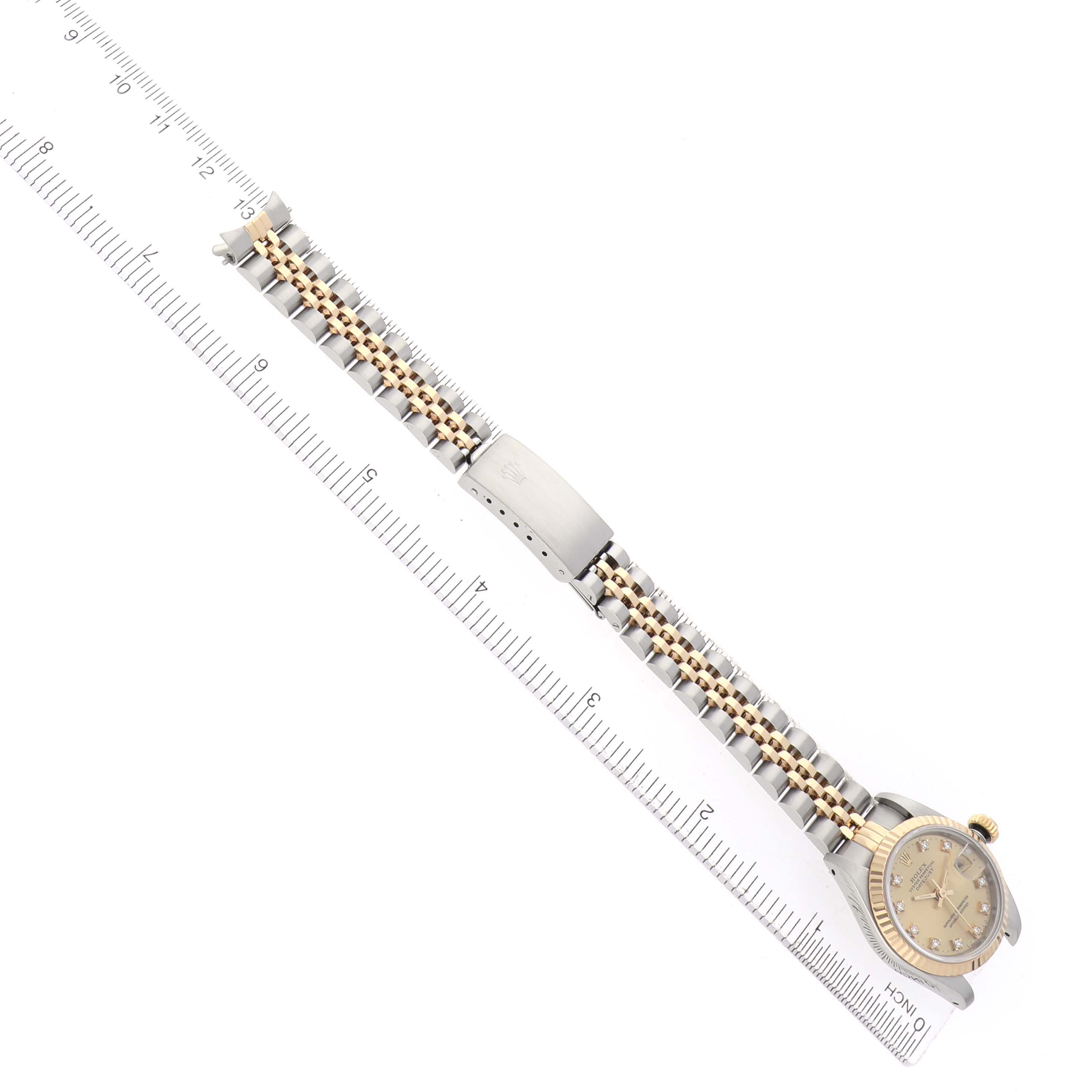 The Rolex Datejust 69173 Women
s Steel and Gold (two tone) Champagne Dial watch is shown from a top view, displaying the face, bezel, bracelet, and clasp with a ruler for scale.