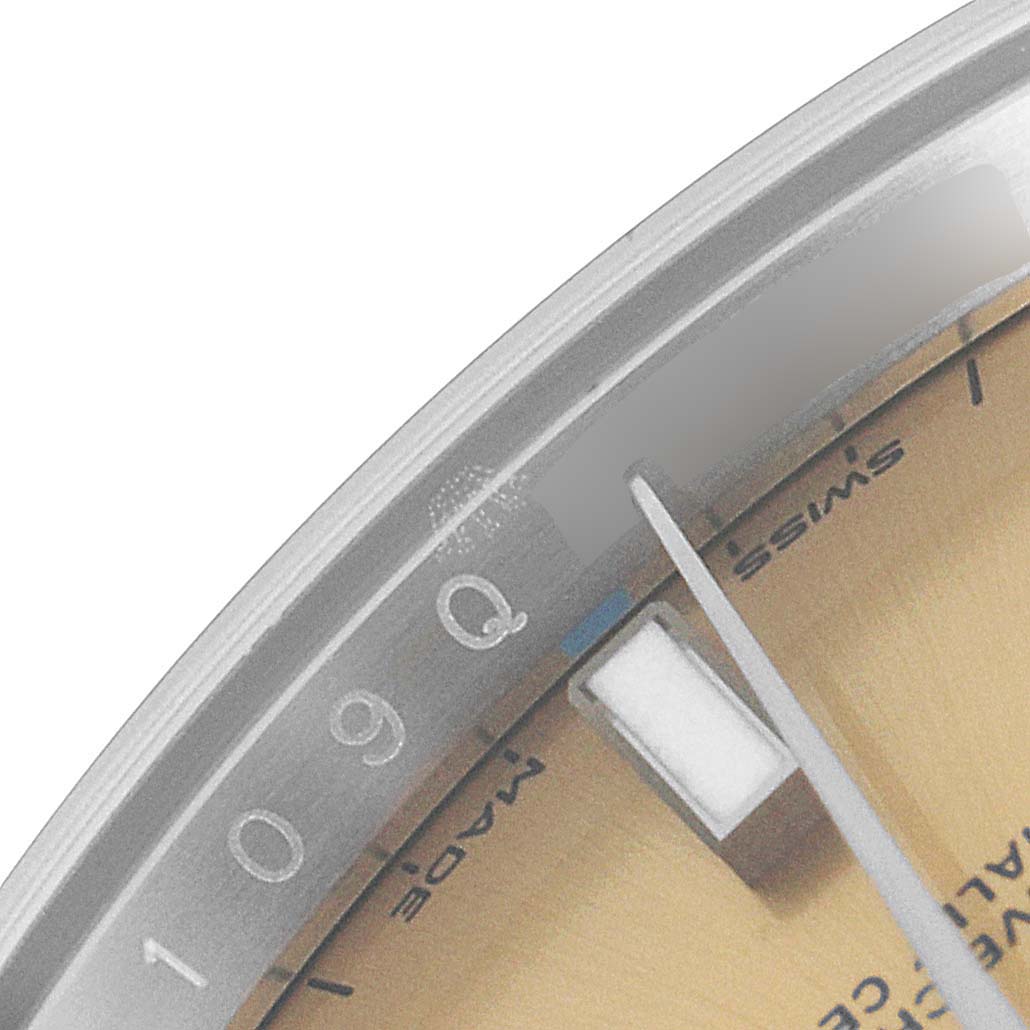 This close-up image of the Rolex Oyster Perpetual 114200 Men's Stainless Steel Champagne Dial 114200 Men's Stainless Steel Champagne Dial watch shows a portion of the dial and hands at an angled view.