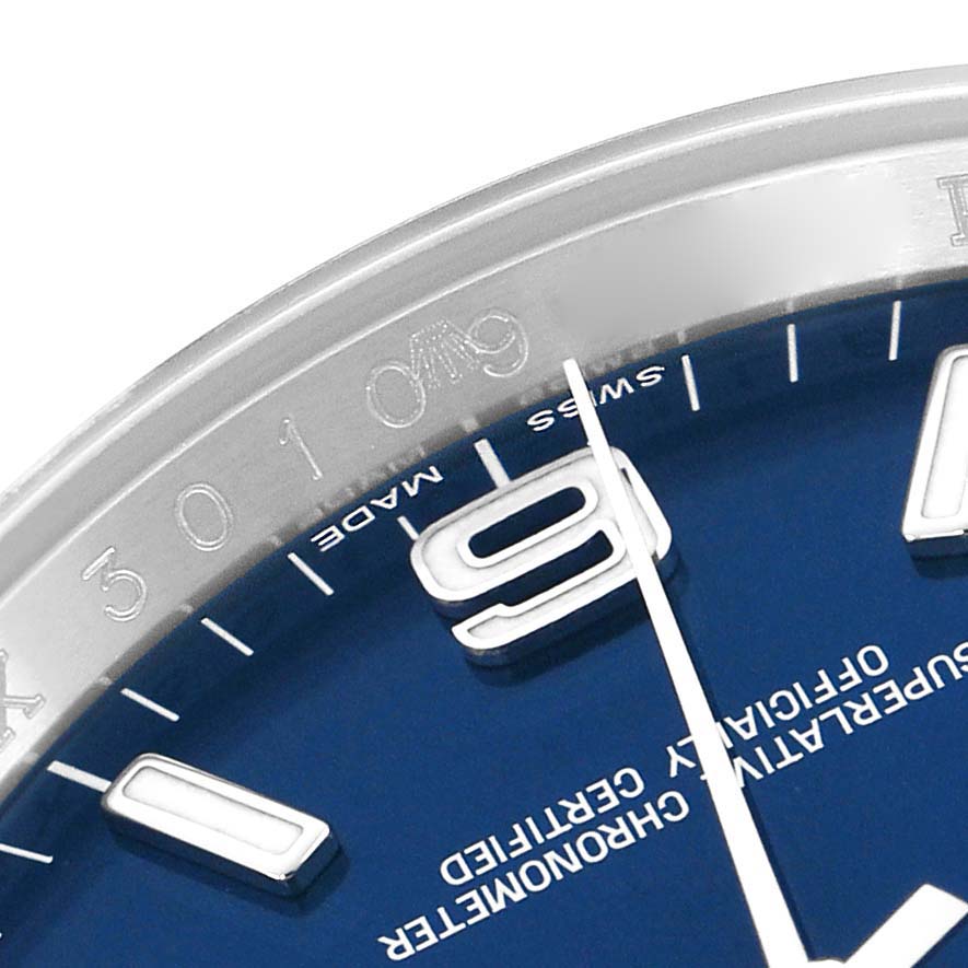 The image shows a close-up of the dial and bezel of a Rolex Oyster Perpetual 116000 Men's Stainless Steel Blue Dial watch, highlighting the numerals and text.