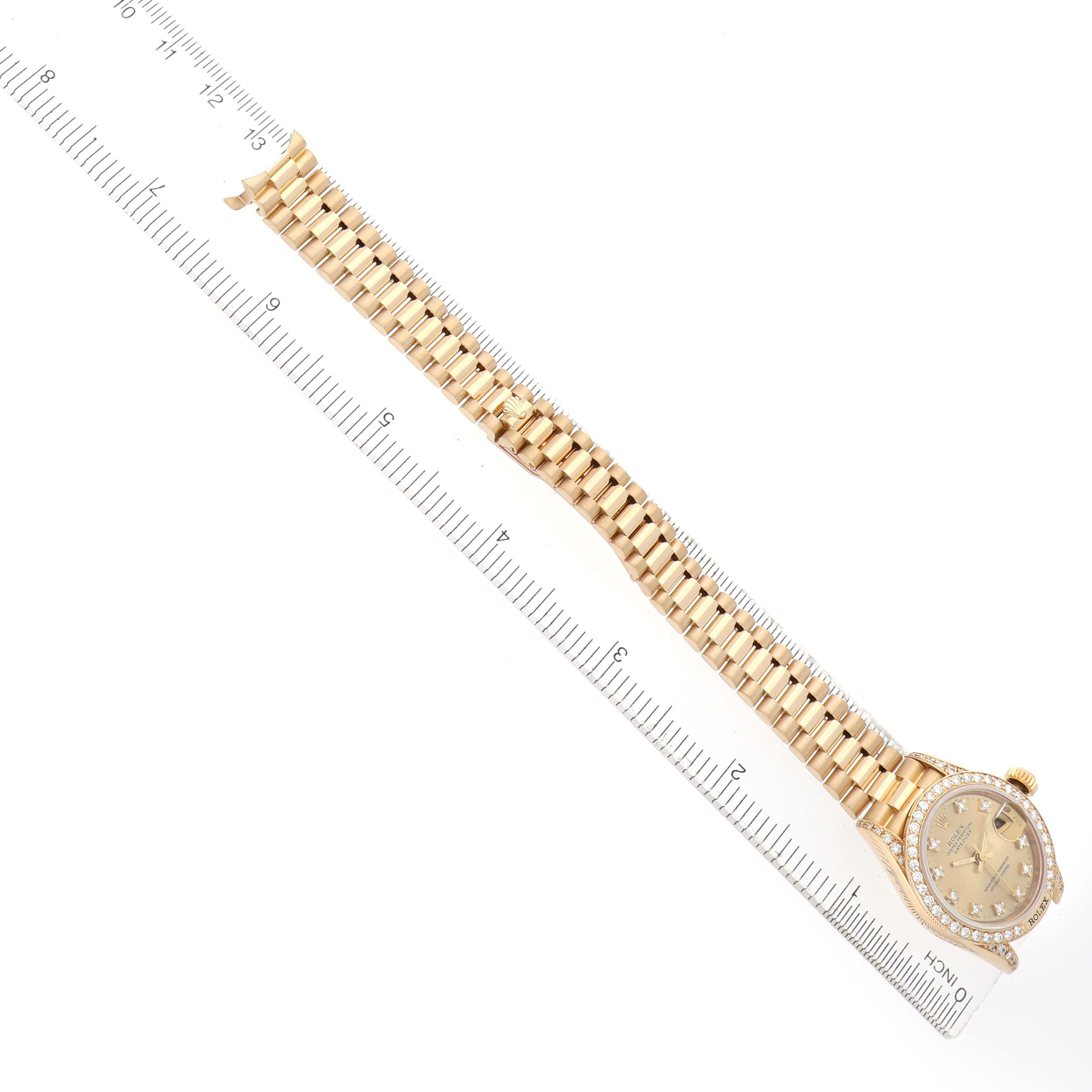 The image shows a Rolex President 69158 Women
s Yellow Gold Champagne Dial model watch from a top-down angle, displaying the full bracelet and watch face with a ruler beside it.