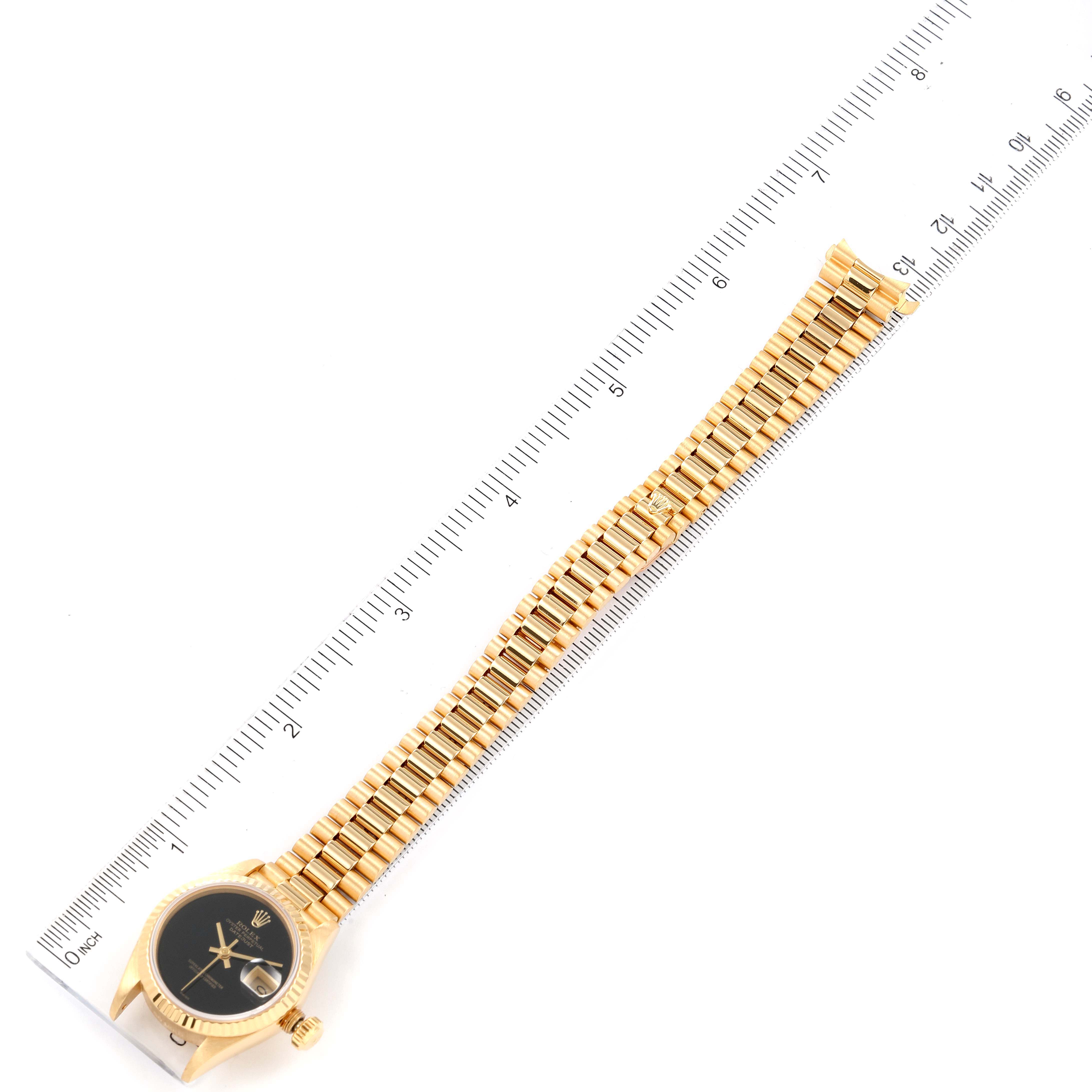 The image shows the entire Rolex President 69178 Women's Yellow Gold Black Dial 69178 Women's Yellow Gold Black Dial watch laid flat next to a ruler for scale.