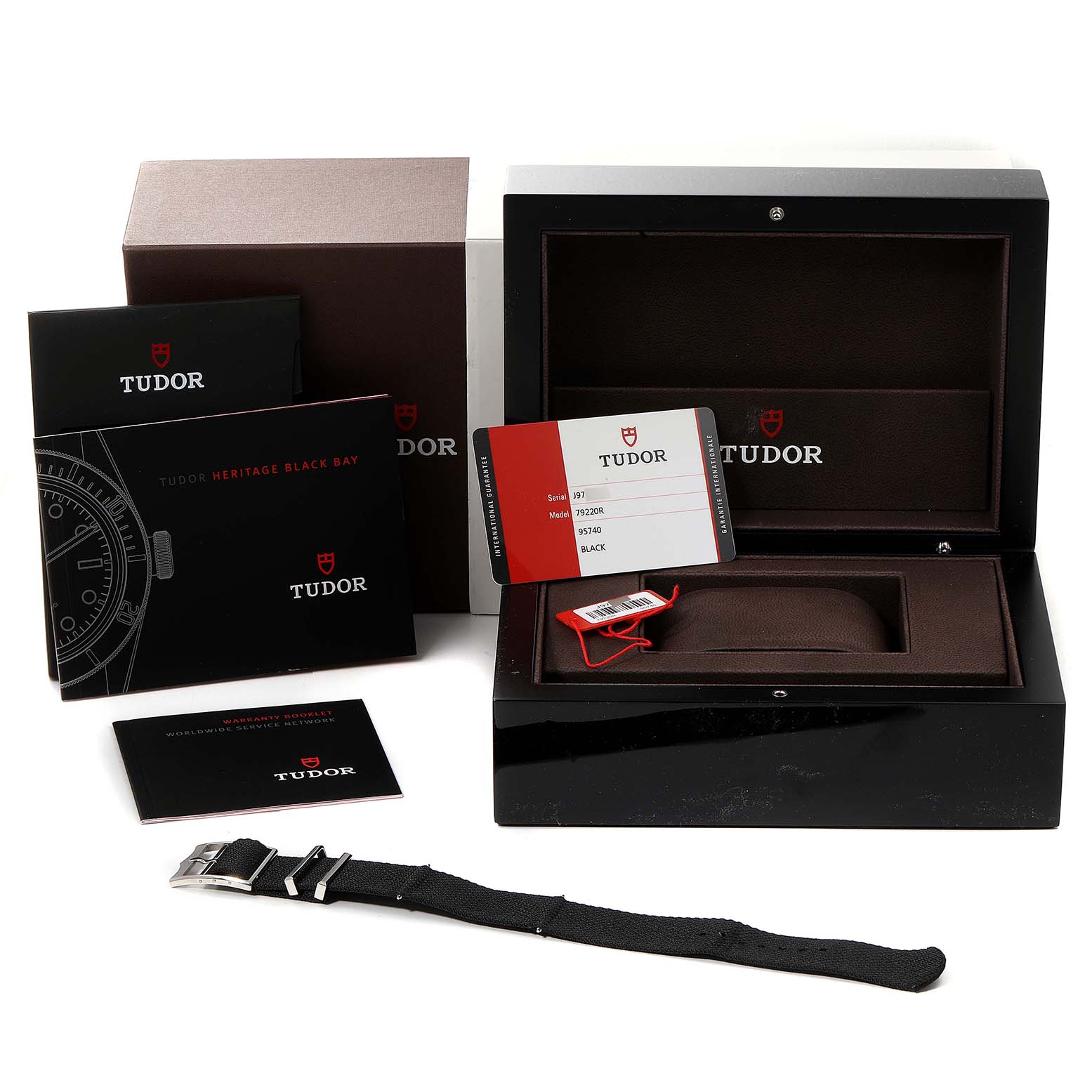 The image shows packaging and accessories for the Tudor Heritage Black Bay 79220R Men's Stainless Steel Black Dial 79220R Men's Stainless Steel Black Dial model, including the box, manuals, warranty card, and an extra strap.