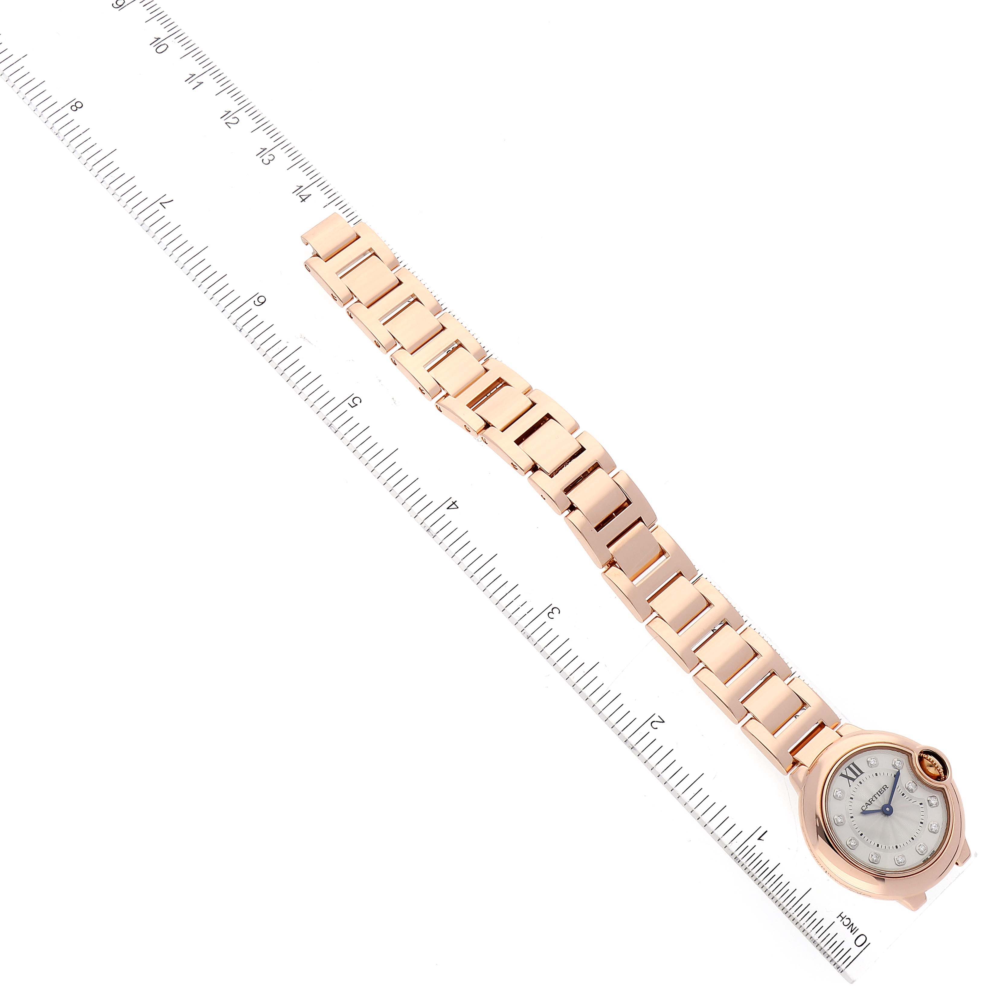 This image shows the Cartier Ballon Bleu WE902025 Women's Rose Gold Silver Dial WE902025 Women's Rose Gold Silver Dial watch with a golden bracelet, positioned diagonally alongside a ruler.