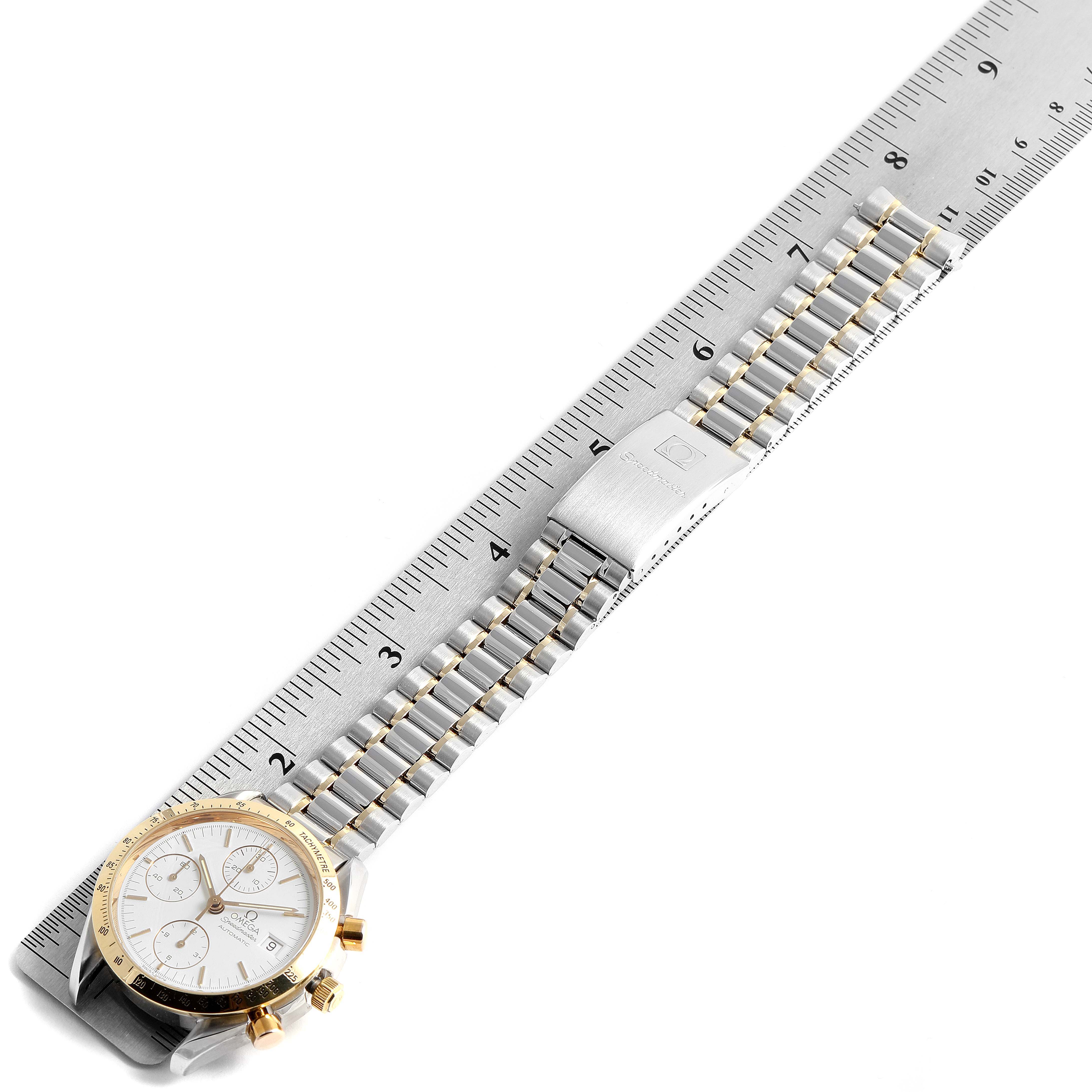 This image shows an Omega Speedmaster 3311.20.00 Men's Steel and Gold (two tone) White Dial 3311.20.00 Men's Steel and Gold (two tone) White Dial watch laid flat next to a ruler, highlighting the dial, bezel, and bracelet.