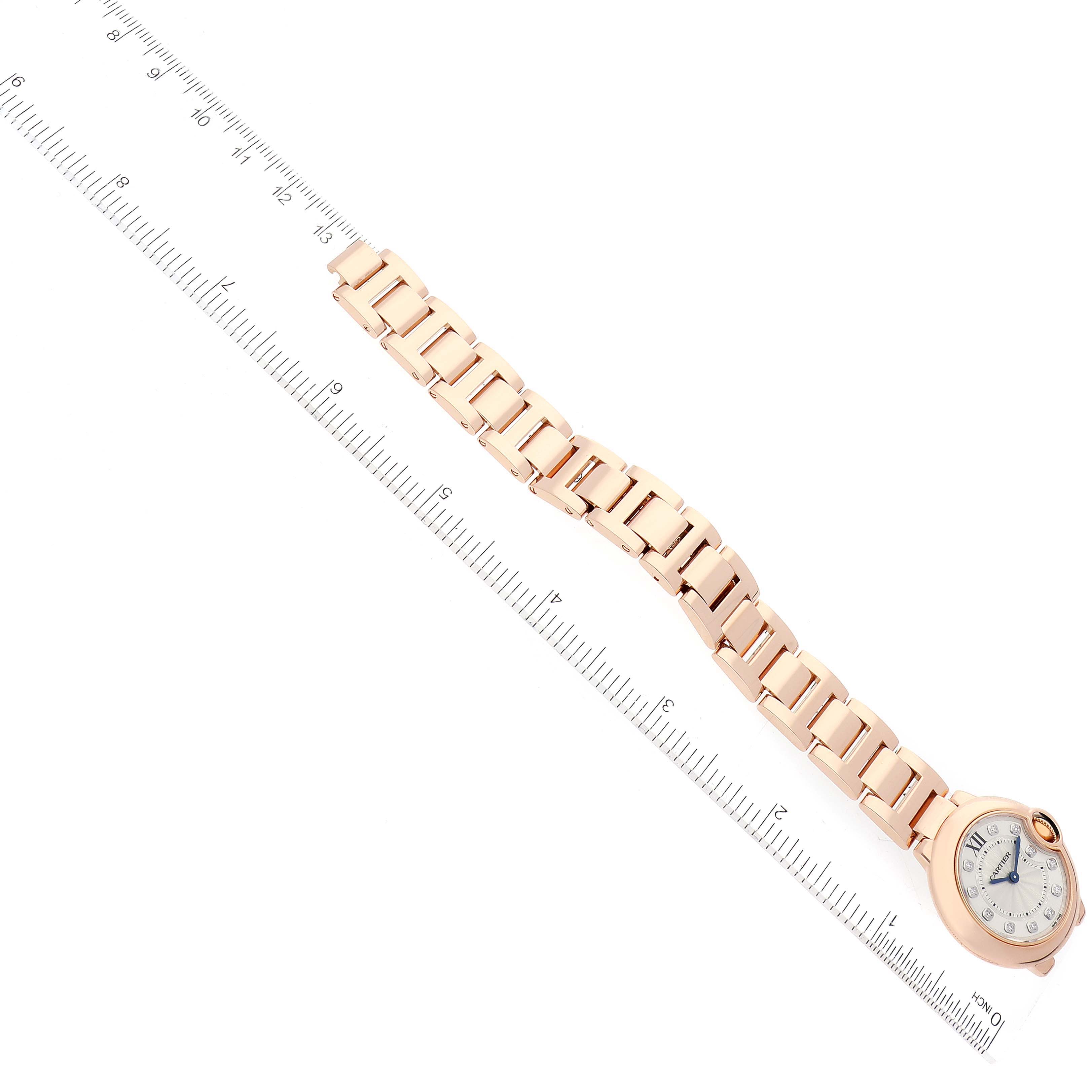 The image shows a Ballon Bleu de Cartier watch laid flat next to a ruler, highlighting the bracelet and watch face.