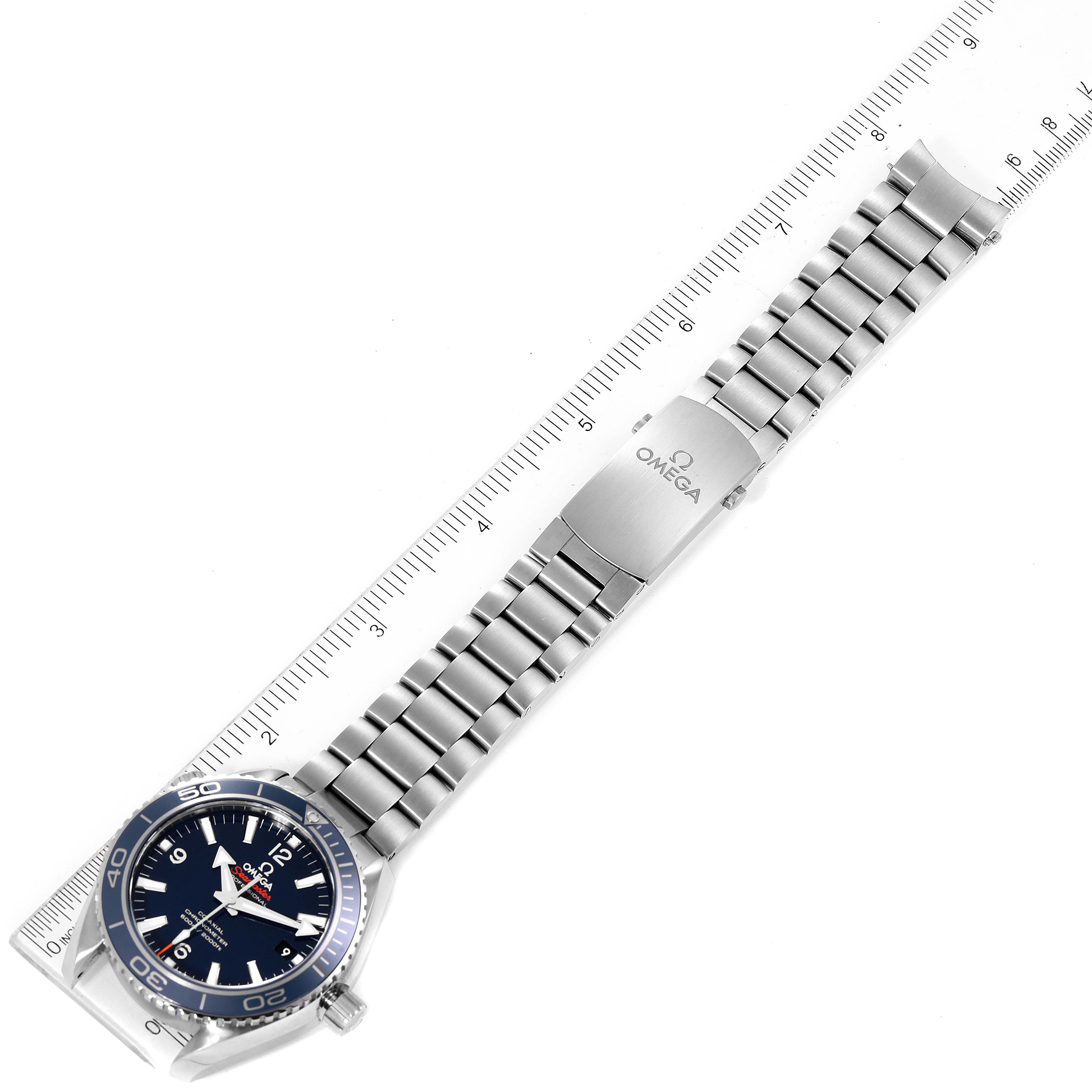 The Omega Planet Ocean 232.90.42.21.03.001 Men's Titanium Blue Dial 232.90.42.21.03.001 Men's Titanium Blue Dial watch is shown laid flat, face-up, alongside a ruler, highlighting its bracelet.
