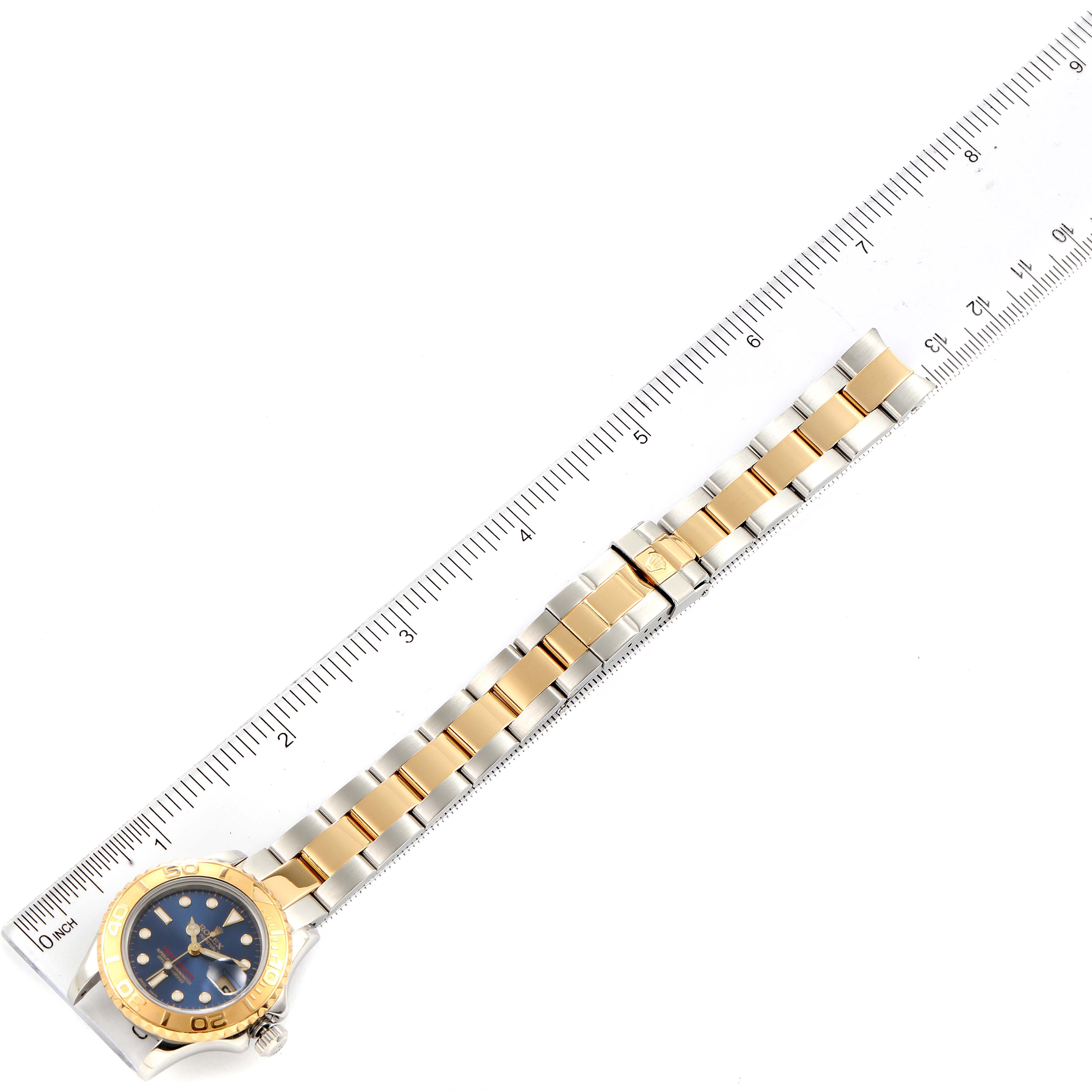 The Rolex Yacht-Master 169623 Women's Steel and Gold (two tone) Blue Dial 169623 Women's Steel and Gold (two tone) Blue Dial watch is shown from an overhead angle alongside a ruler, showcasing its bracelet and face.