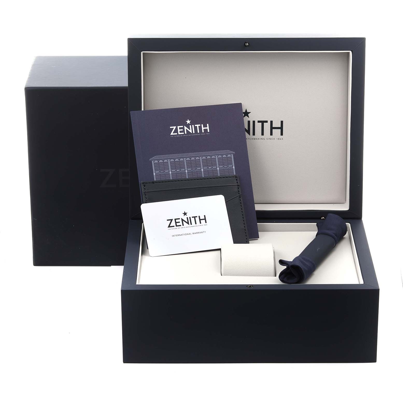 The image shows a Zenith Chronomaster 03.3119.3600/56.M3100 Men
s Stainless Steel Green Dial 03.3119.3600/56.M3100 Men
s Stainless Steel Green Dial watch box containing manuals, a warranty card, and a cleaning cloth.