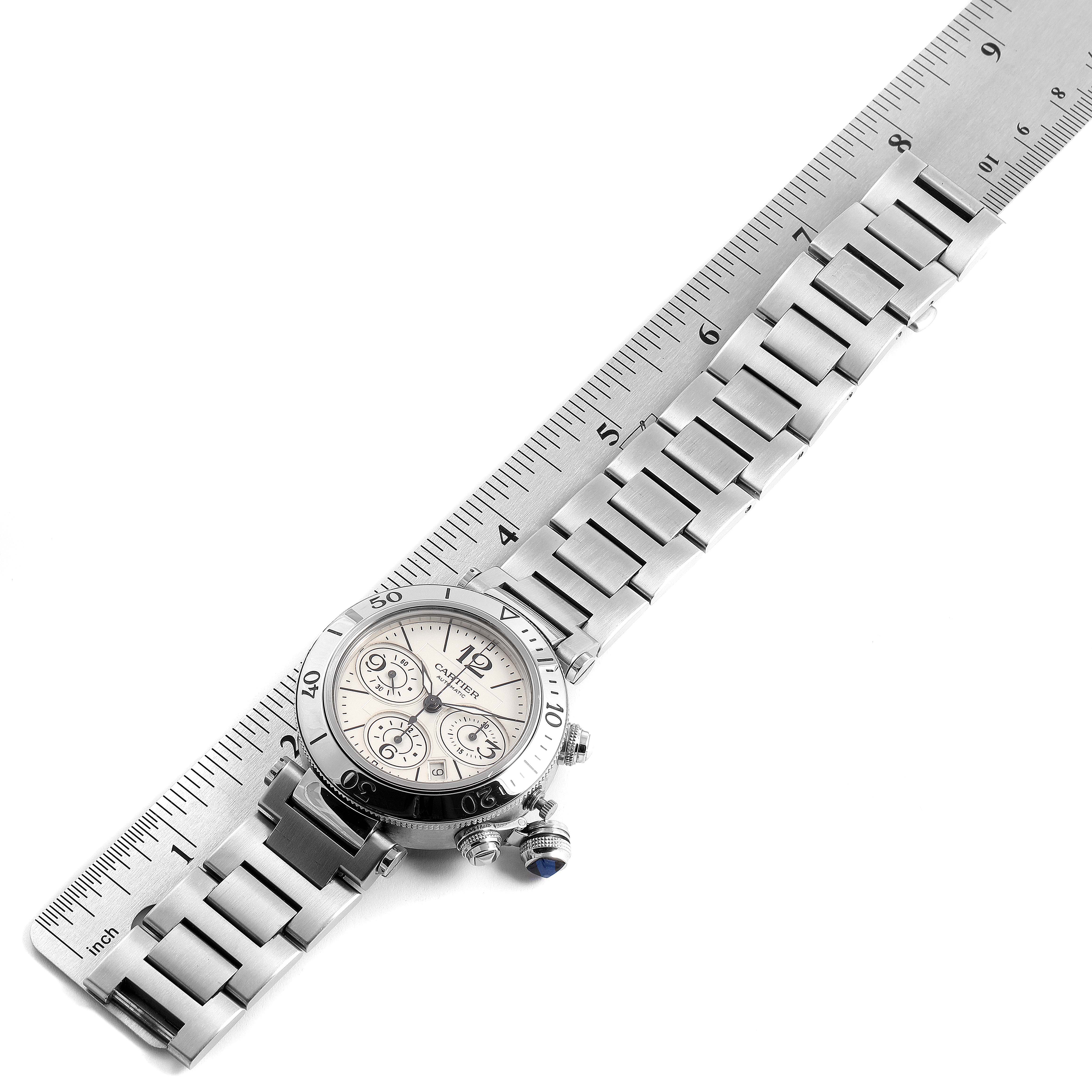 The image shows a top-down view of a Cartier Pasha W31089M7 Men's Stainless Steel Silver Dial W31089M7 Men's Stainless Steel Silver Dial watch with its metal bracelet aligned alongside a ruler for measurement.