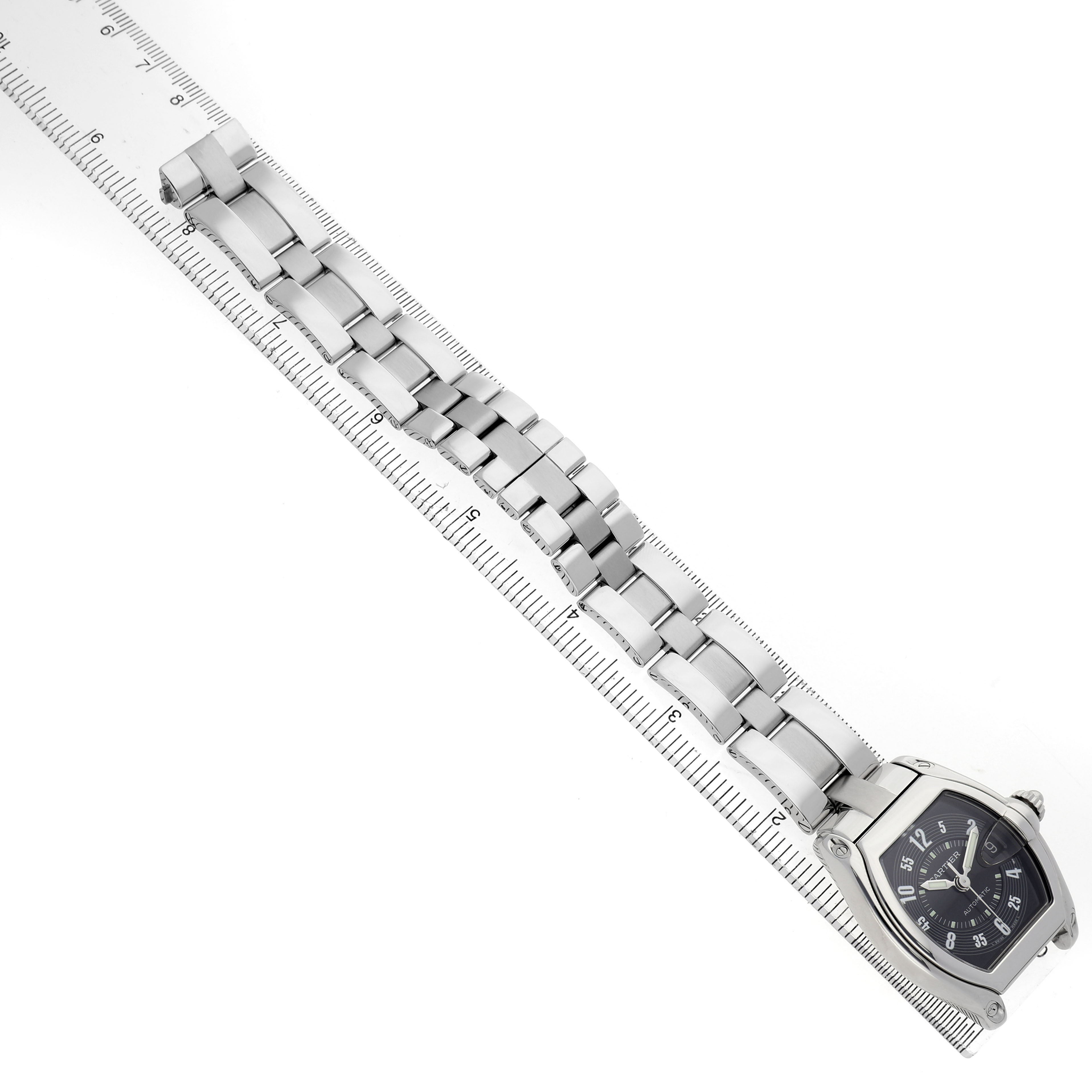 The Cartier Roadster W62004V3 Men's Stainless Steel Black Dial watch is shown from a top angle, highlighting the face and stainless steel bracelet next to a ruler.