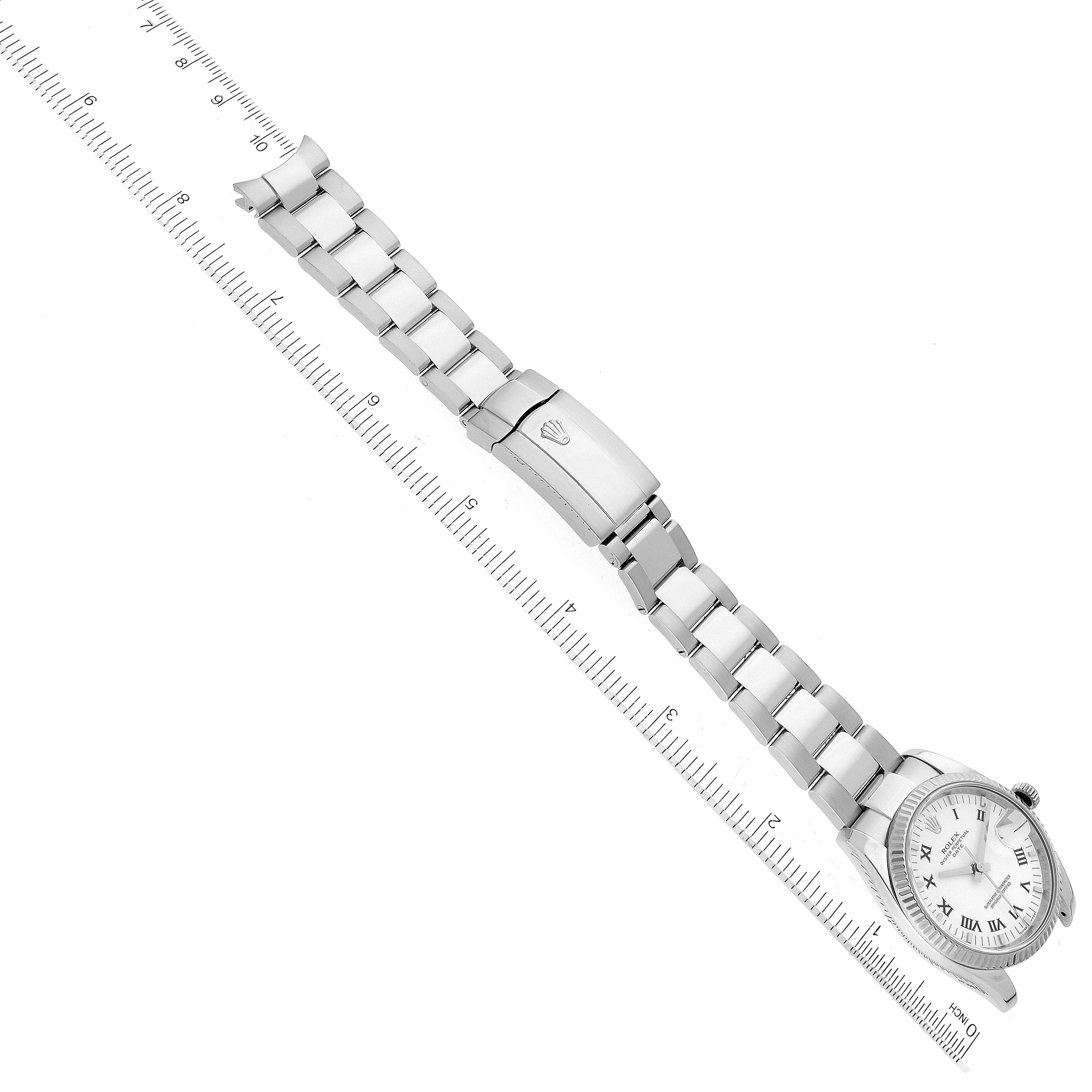 The Rolex Date 115234 Men's Stainless Steel White Dial 115234 Men's Stainless Steel White Dial model watch is shown from an overhead perspective, displaying its bracelet and clasp alongside a ruler for scale.
