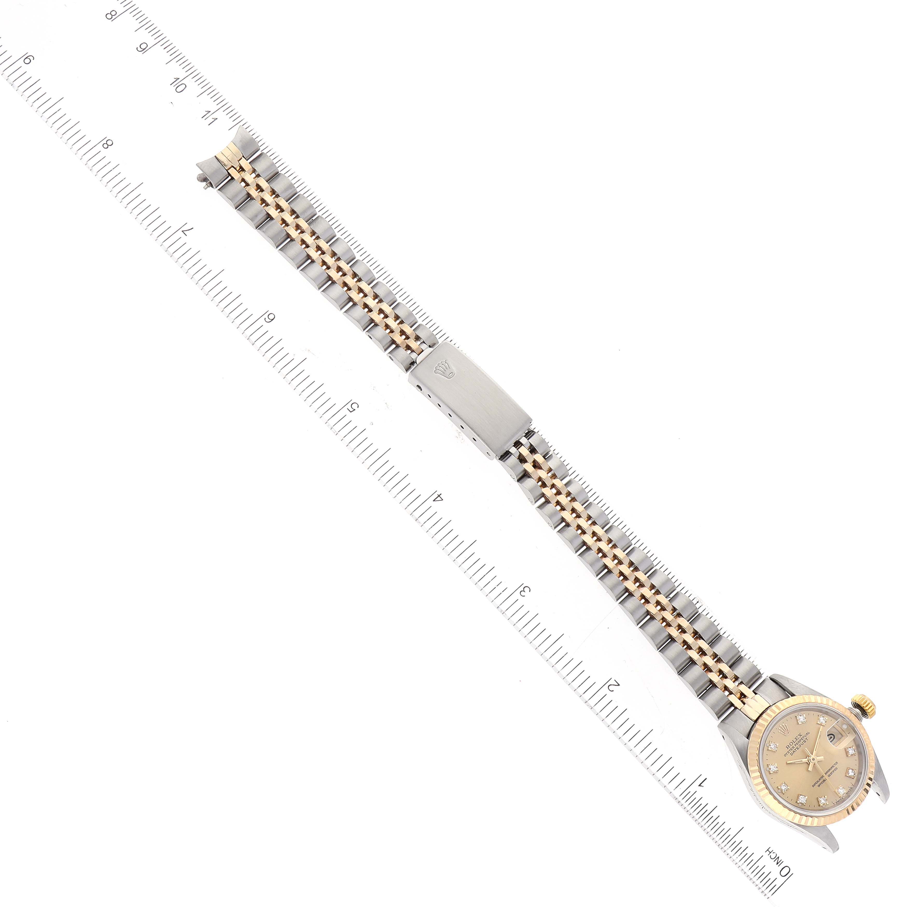 This image shows an overhead view of a Rolex Datejust 69173 Women's Steel and Gold (two tone) Champagne Dial 69173 Women's Steel and Gold (two tone) Champagne Dial watch, featuring its dial, bezel, and two-tone bracelet partially covering a ruler.