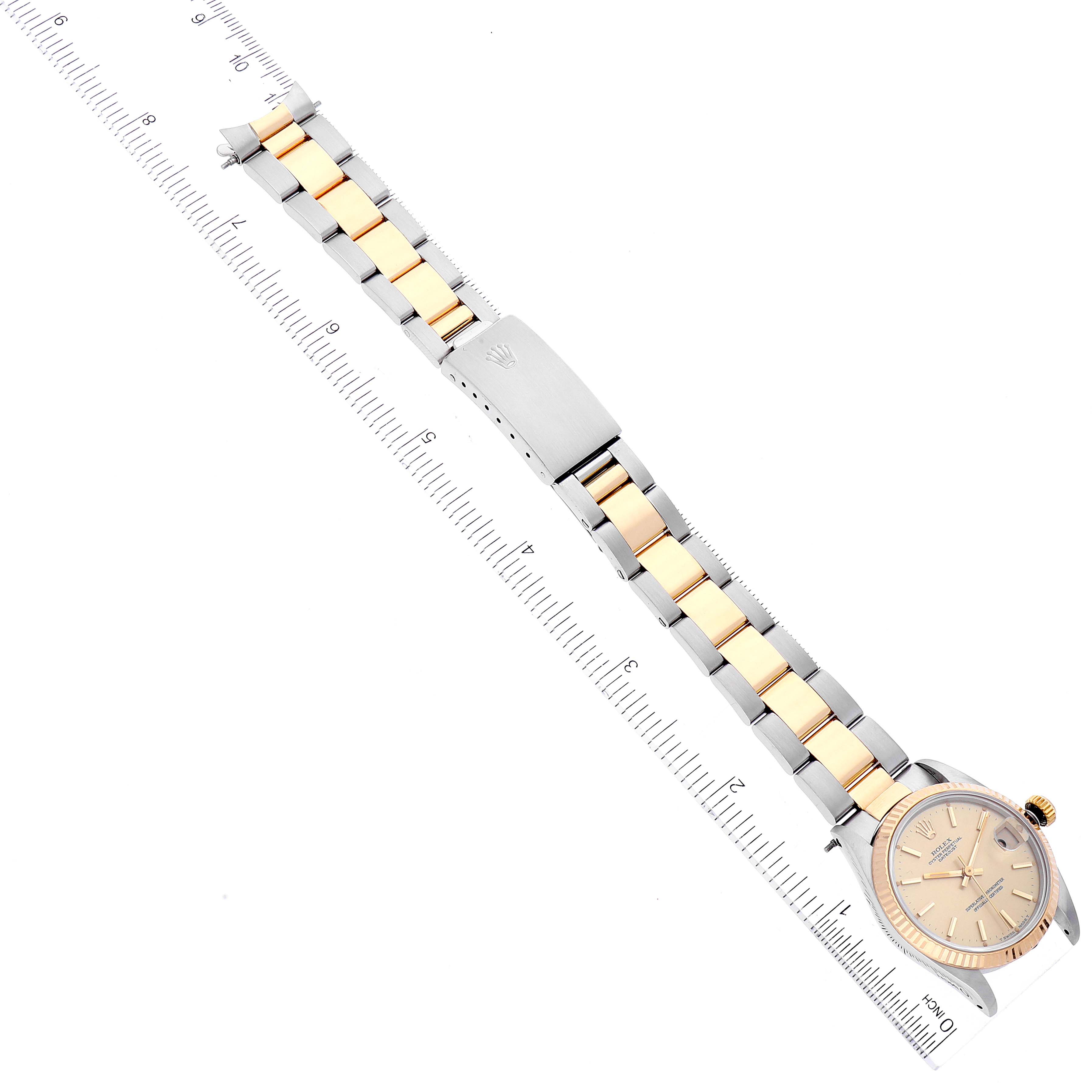 This image shows a top-down view of a Mid-Size Rolex watch, featuring its face, gold and silver bracelet, and clasp, measured against a ruler.