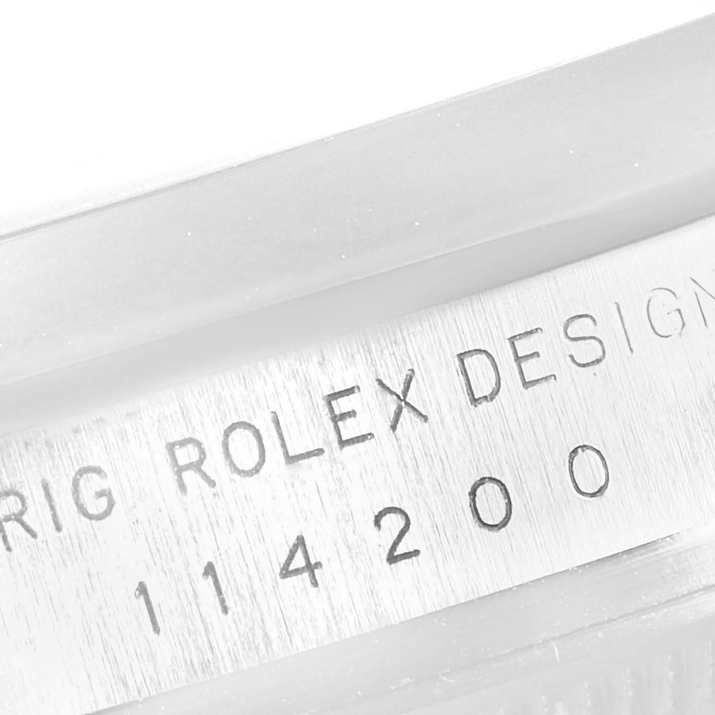 This is a close-up of the case side of a Rolex Oyster Perpetual 114200 Men's Stainless Steel Champagne Dial 114200 Men's Stainless Steel Champagne Dial watch, showing the model number 114200 and "ROLEX DESIGN" engraving.