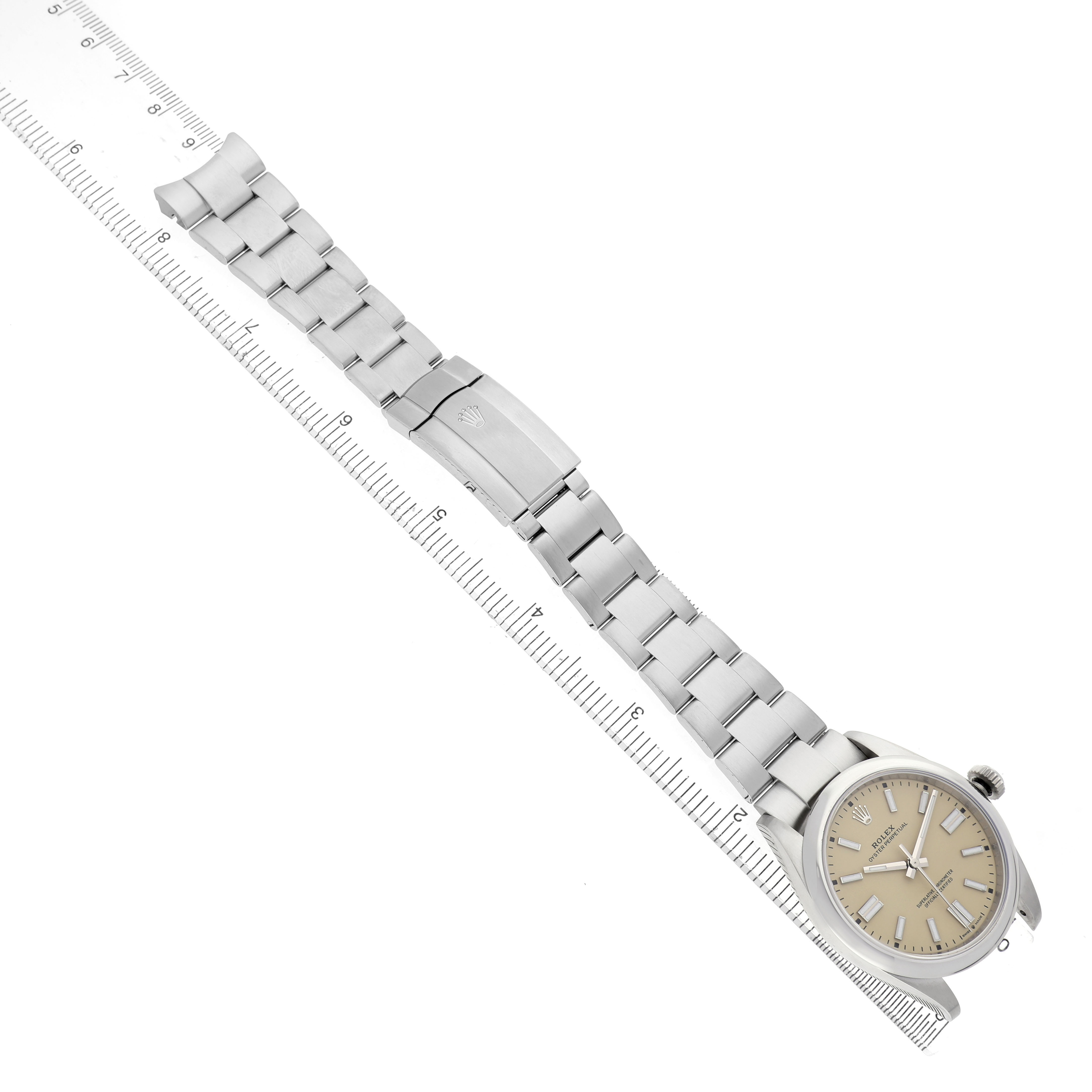 The Rolex Oyster Perpetual 134300 Men's Stainless Steel Beige Dial watch is shown at an angle highlighting its bracelet and clasp, with a ruler for scale.
