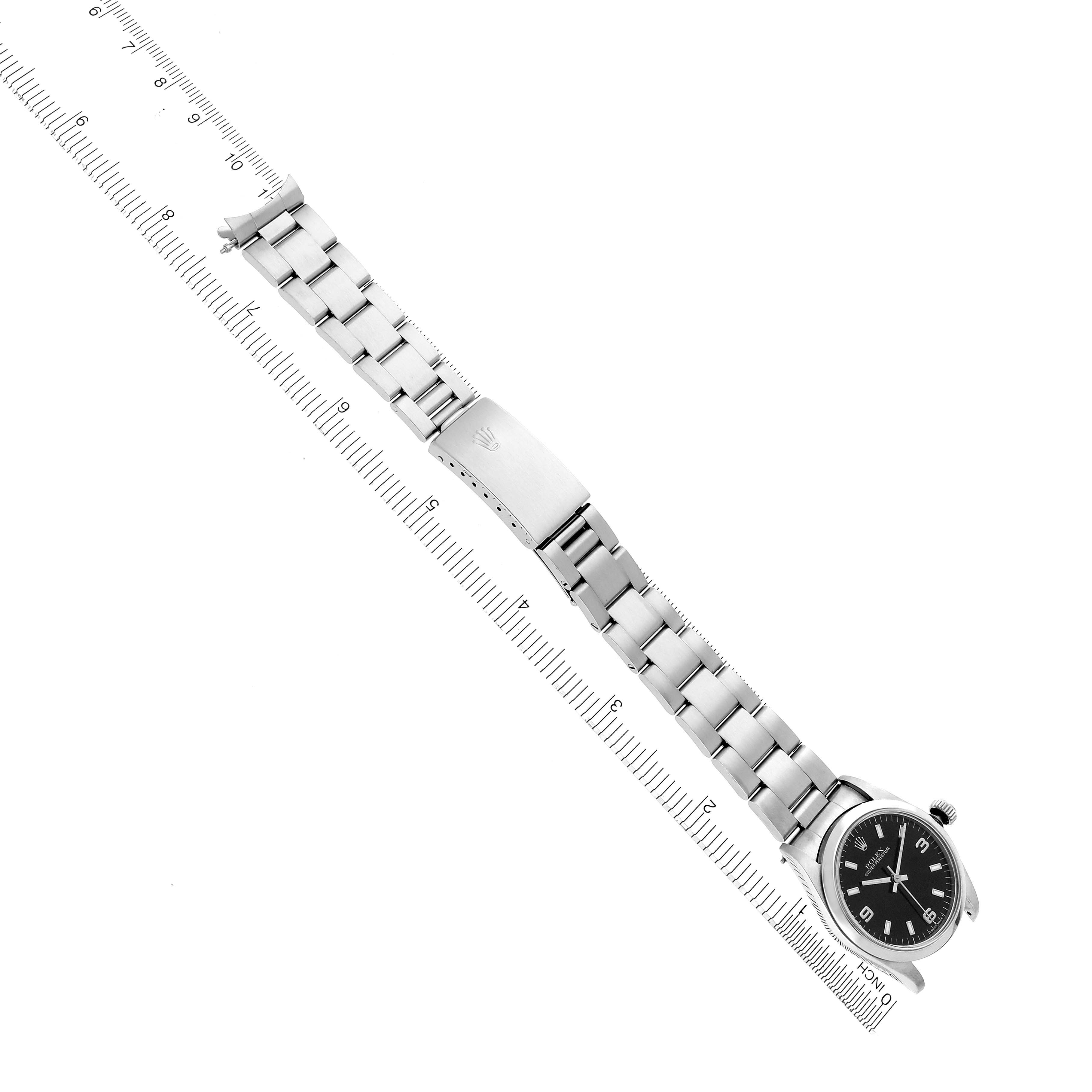 The Rolex Mid-Size 67480 Women's Stainless Steel Black Dial 67480 Women's Stainless Steel Black Dial watch is shown from a top view, displaying its full bracelet, clasp, and face alongside a ruler.