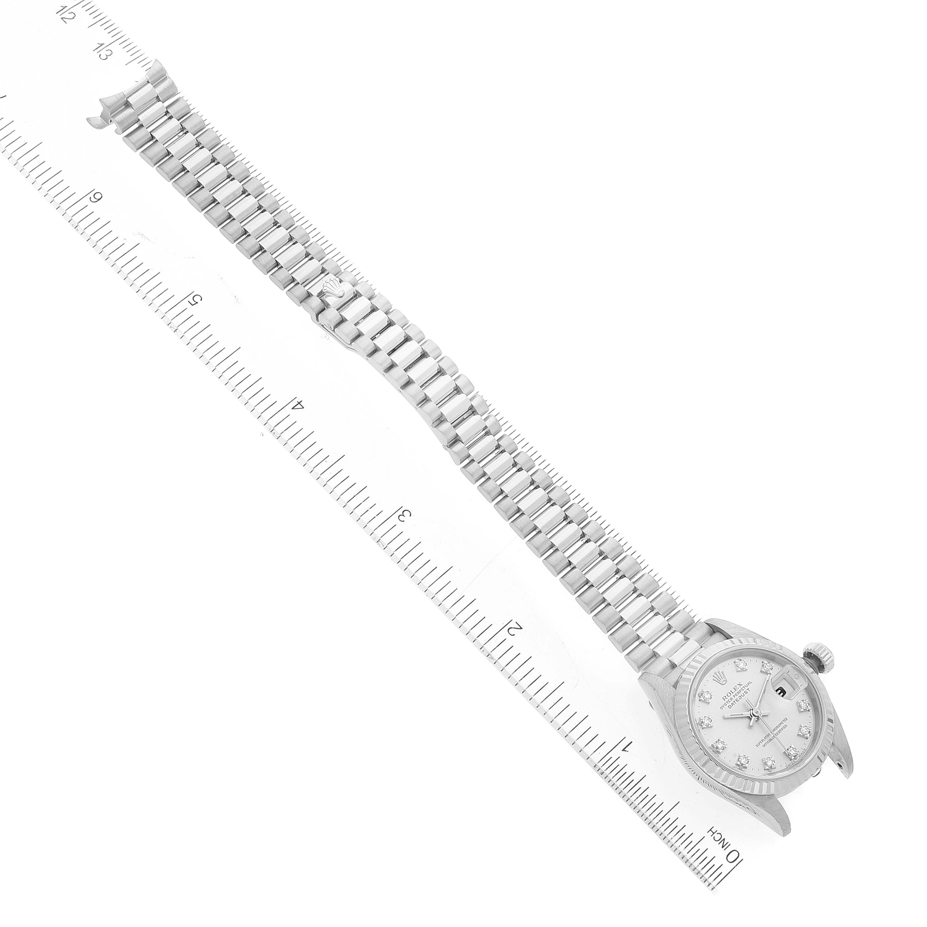 The image shows the full view of a Rolex President 69179 Women's White Gold Silver Dial 69179 Women's White Gold Silver Dial watch, including the face, bracelet, and a portion of its crown, placed alongside a ruler.