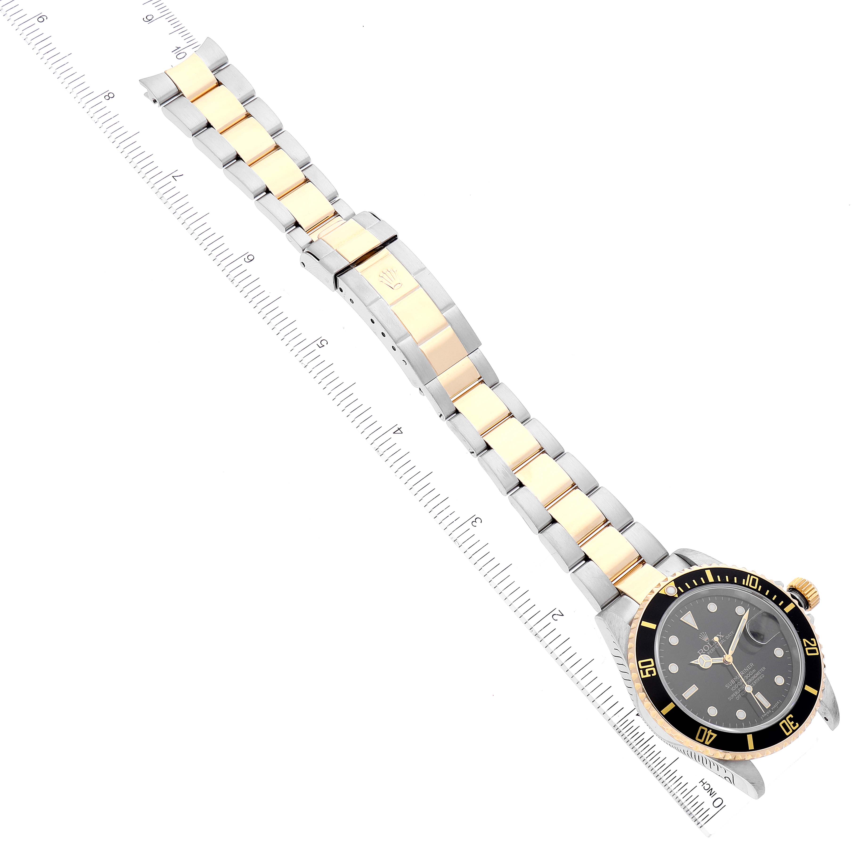 The image shows a Rolex Submariner 16613 Men
s Steel and Gold (two tone) Black Dial 16613 Men
s Steel and Gold (two tone) Black Dial watch laid flat with its bracelet fully extended and a ruler for scale.