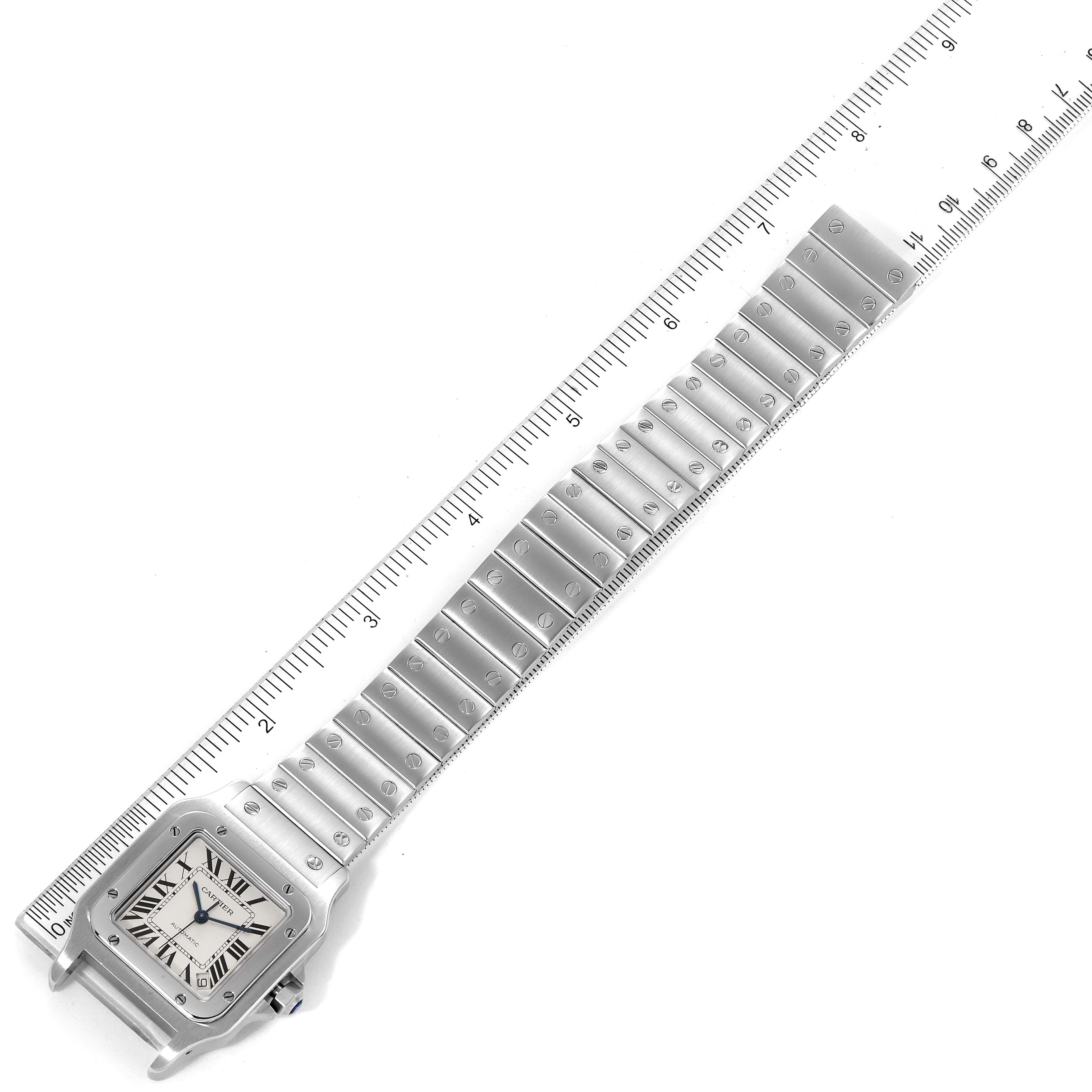The image shows a close-up of a Santos model watch by Cartier, viewed from the top, including the face and entire metal band aligned with a ruler.