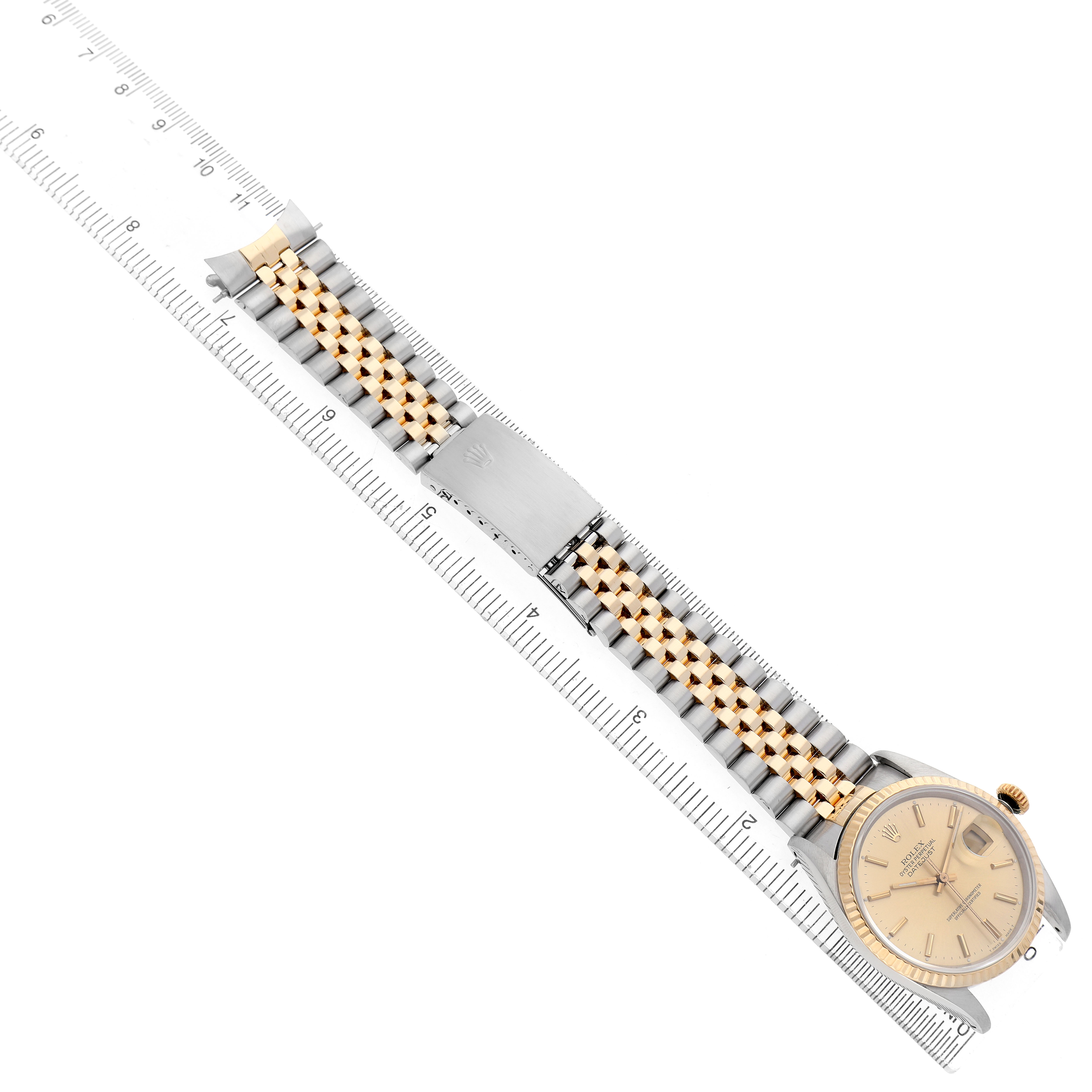 The Rolex Datejust 16233 Men's Steel and Gold (two tone) Champagne Dial watch is shown from a top-down angle, displaying the full face and the entire metal and gold bracelet aligned with a ruler.