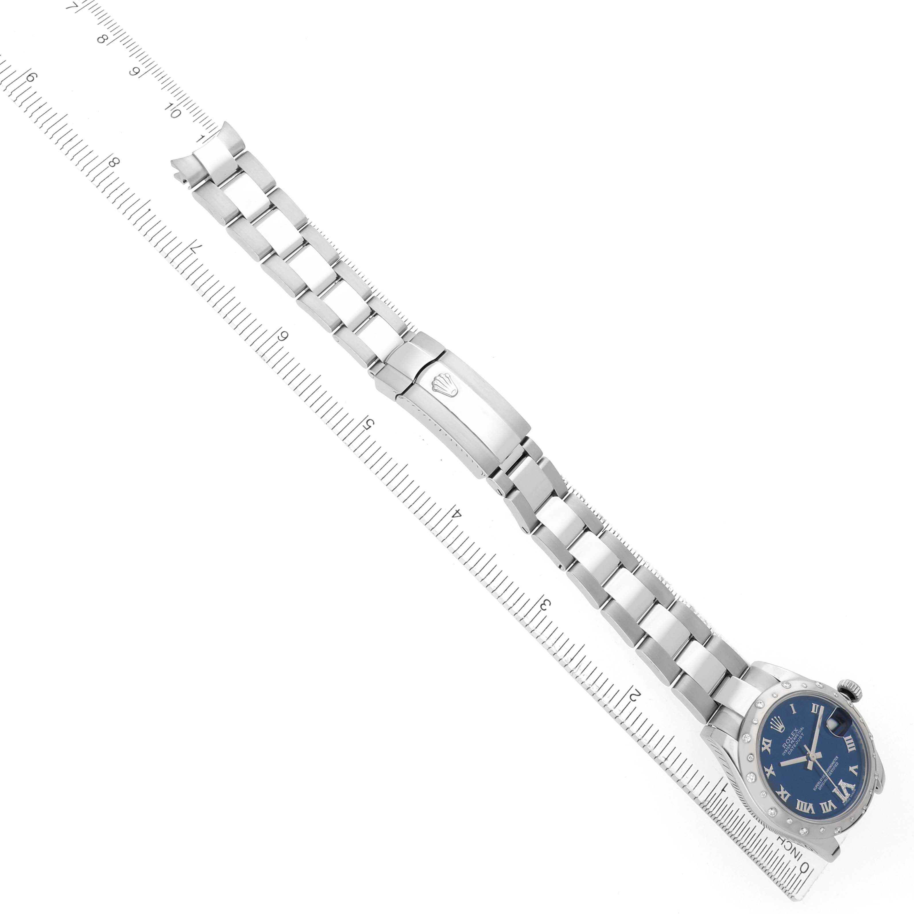 The Rolex Mid-Size 178344 Women
s Stainless Steel Blue Dial watch is displayed diagonally, showing the bracelet, clasp, and a partial view of the dial beside a ruler.