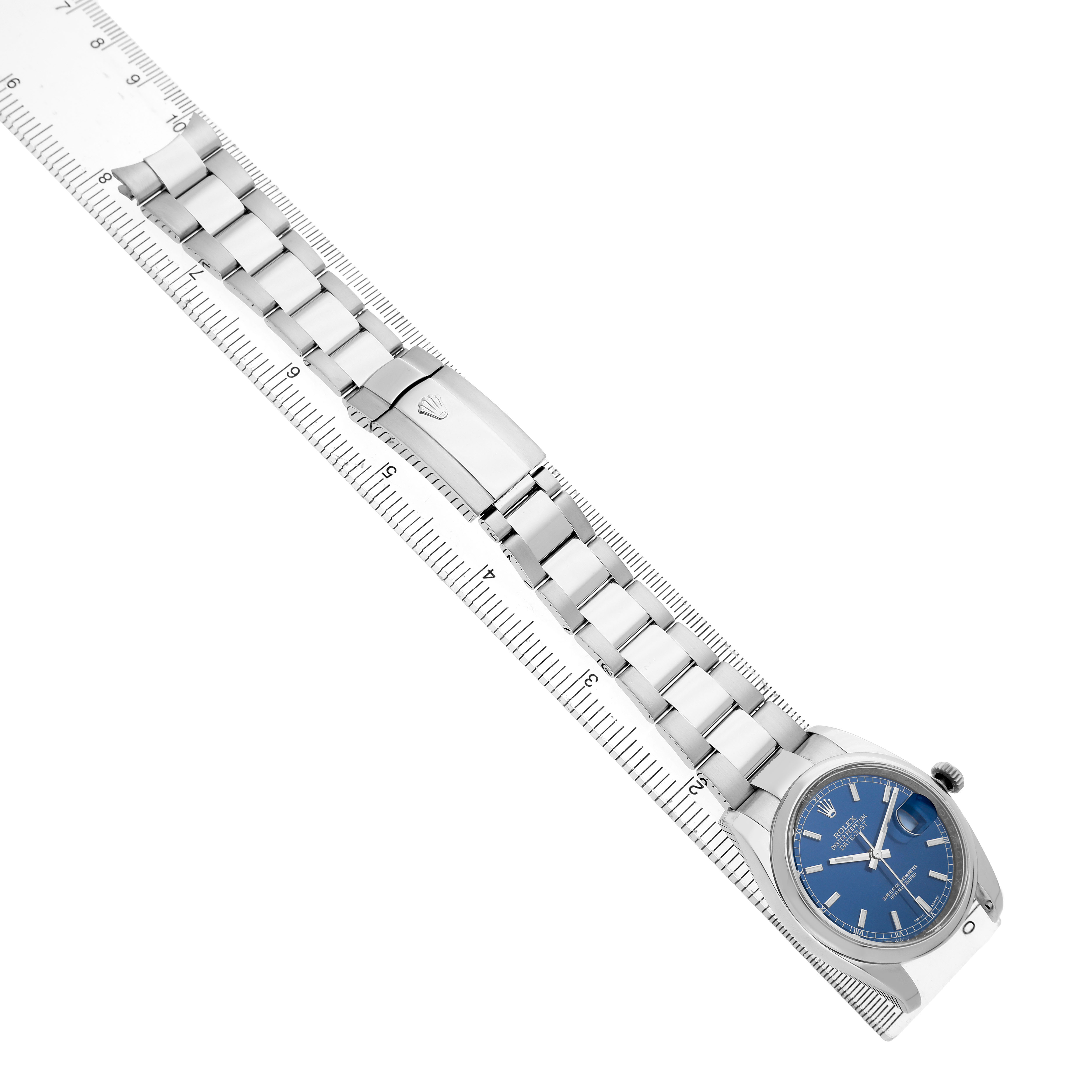 The Rolex Datejust 116200 Men's Stainless Steel Blue Dial watch is shown from an angled top view, highlighting the bracelet, clasp, and face in alignment with a ruler.