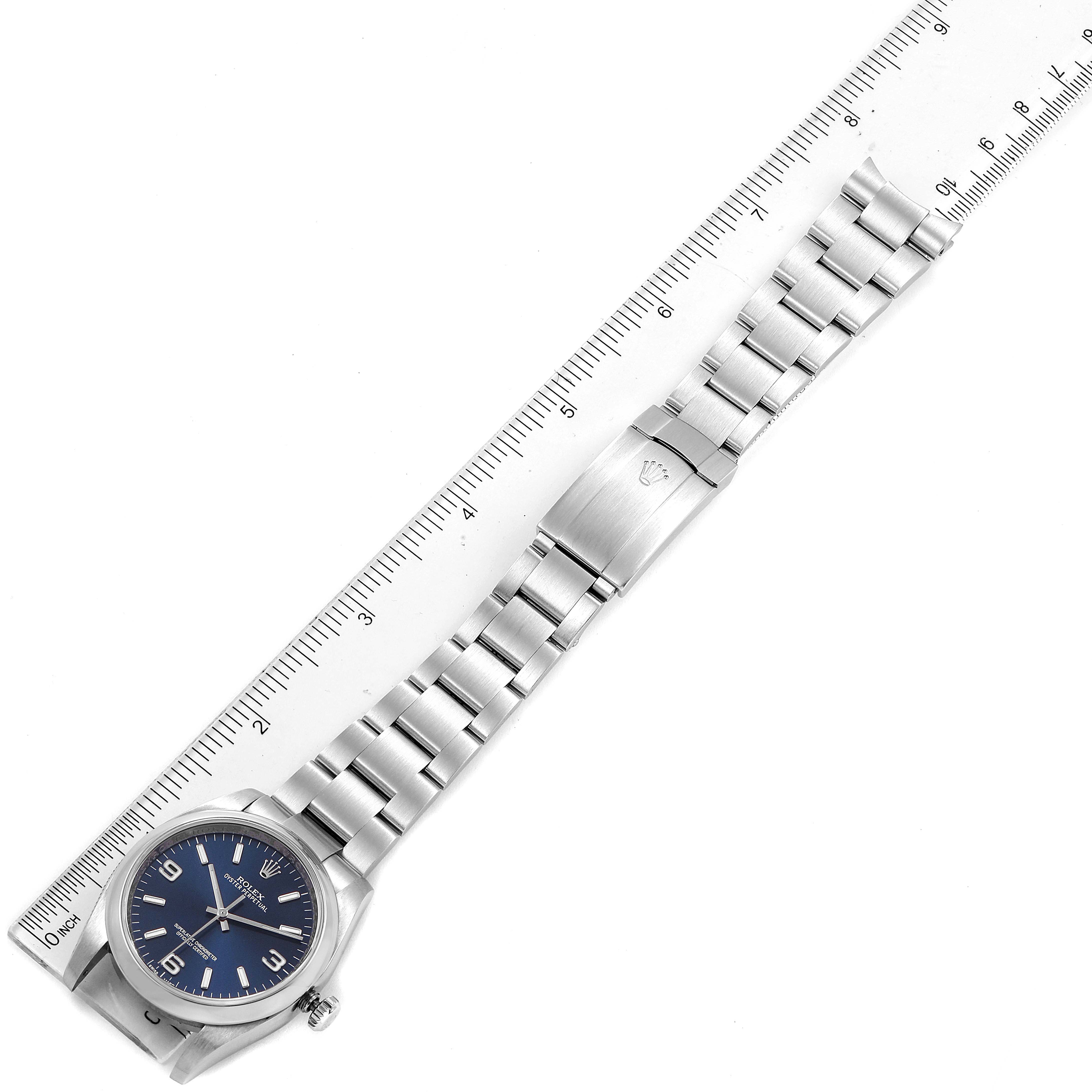 The image shows a Rolex Oyster Perpetual 116000 Men's Stainless Steel Blue Dial 116000 Men's Stainless Steel Blue Dial watch laid flat, displaying the face, bracelet, and clasp with a ruler beside it.