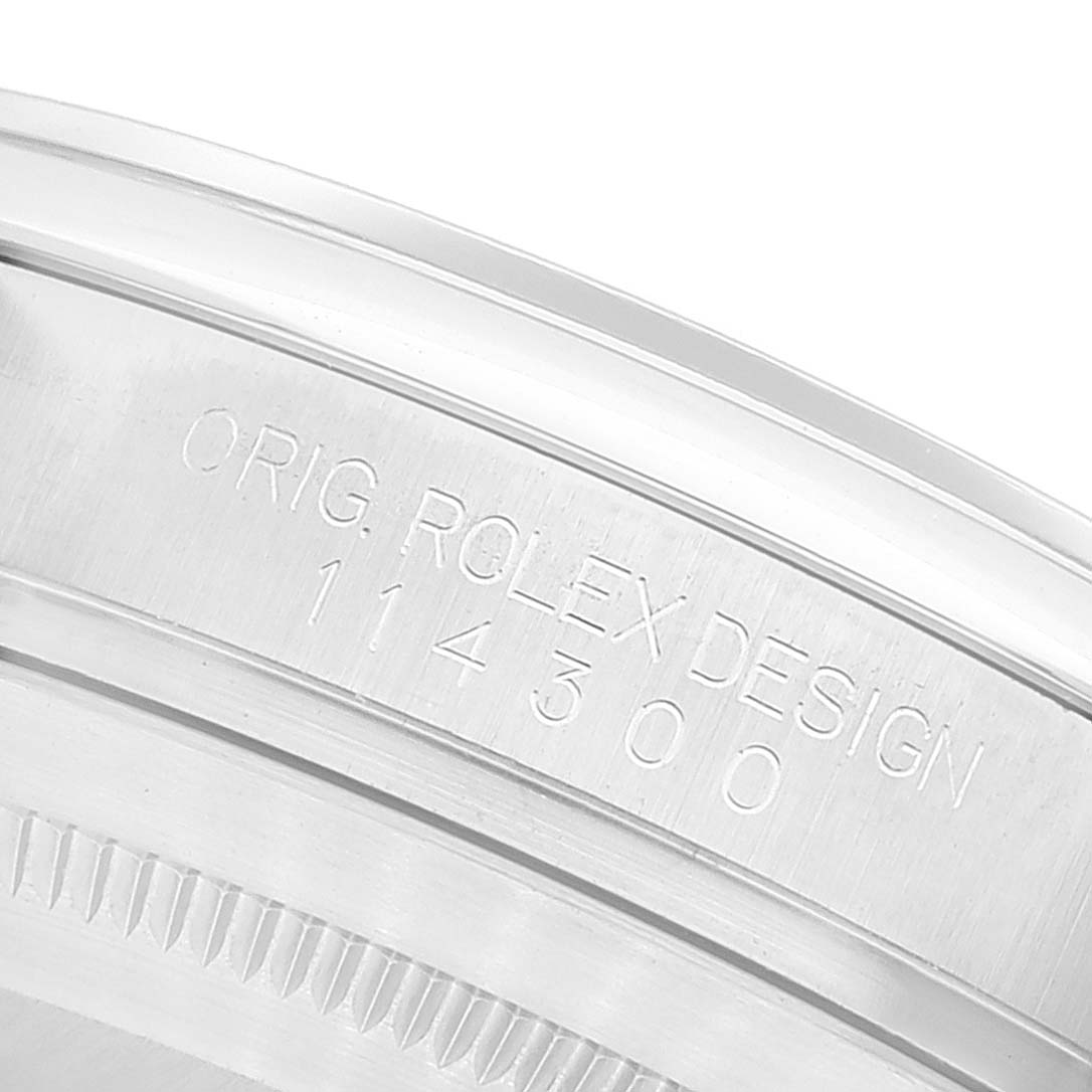 The image shows a close-up of the side of the bezel and engraved serial number of a Rolex Oyster Perpetual 114300 Men's Stainless Steel Burgundy Dial 114300 Men's Stainless Steel Burgundy Dial watch.