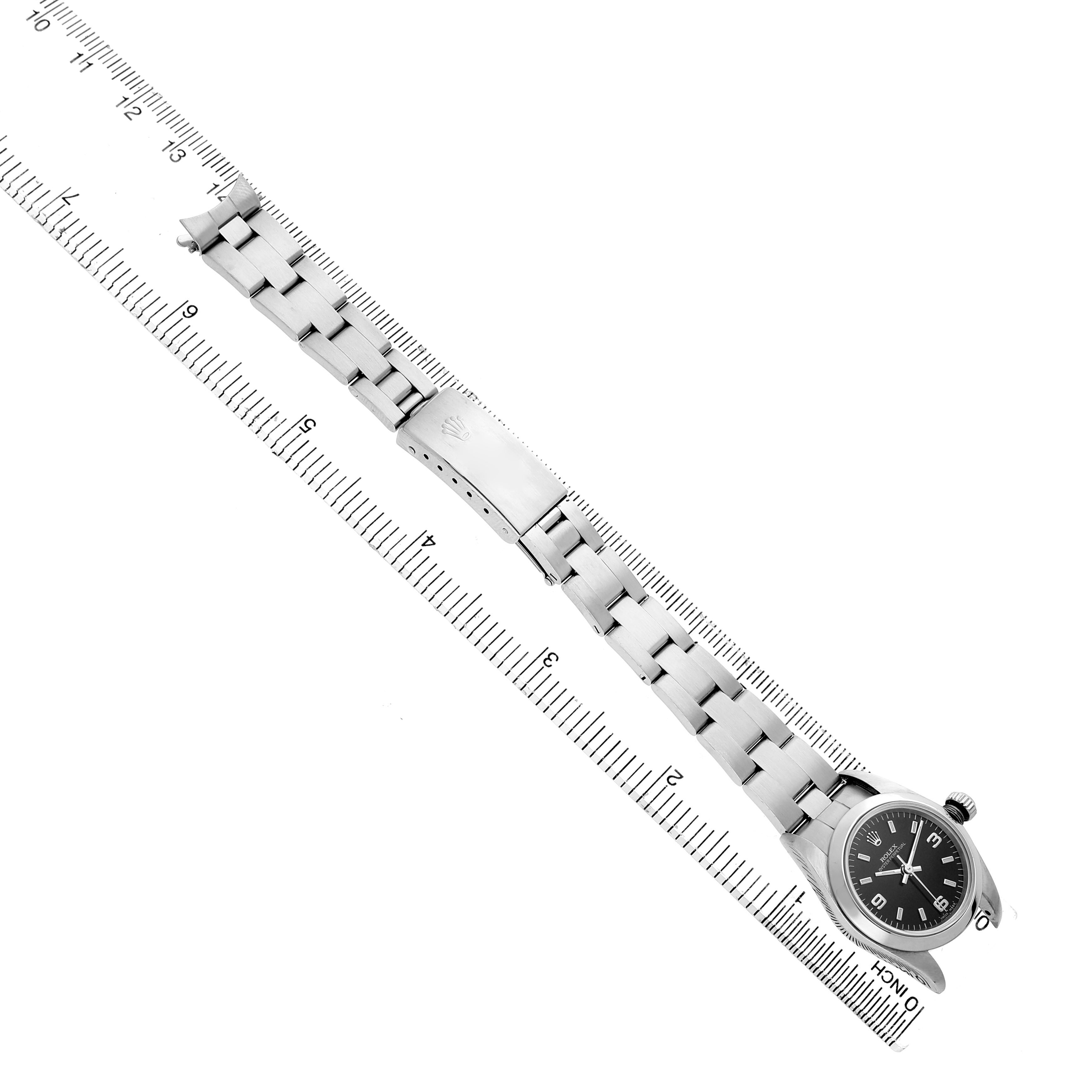 The Rolex Oyster Perpetual 76080 Women's Stainless Steel Black Dial watch is shown from a top-down angle, displaying the bracelet, clasp, and dial next to a ruler.