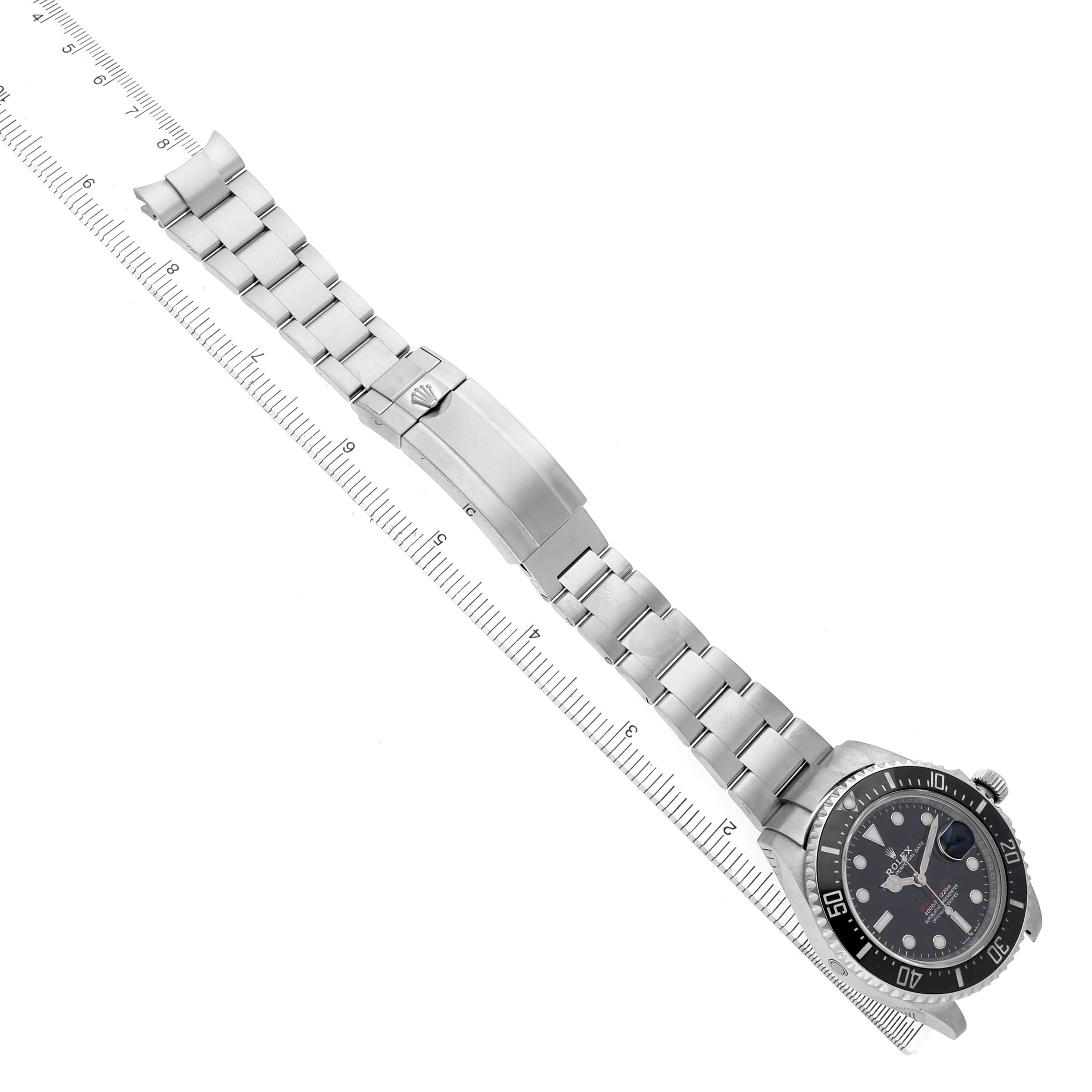 The Rolex Sea-Dweller 126600 Men's Stainless Steel Black Dial watch is shown from an overhead angle, displaying the full bracelet, clasp, and watch face alongside a ruler.