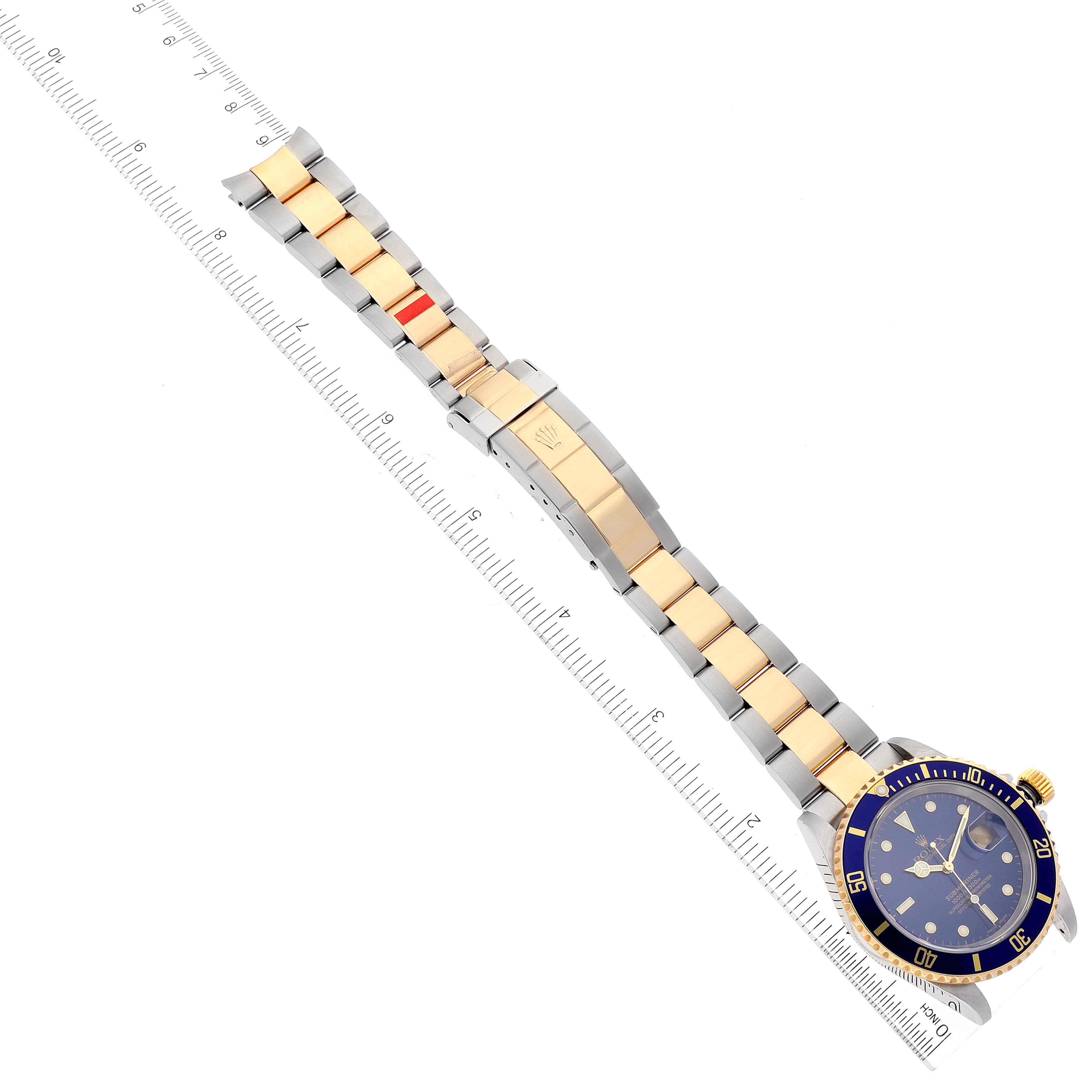 The image shows a top-down view of a Rolex Submariner 16613 Men
s Steel and Gold (two tone) Blue Dial 16613 Men
s Steel and Gold (two tone) Blue Dial watch with its bracelet and a ruler for scale.
