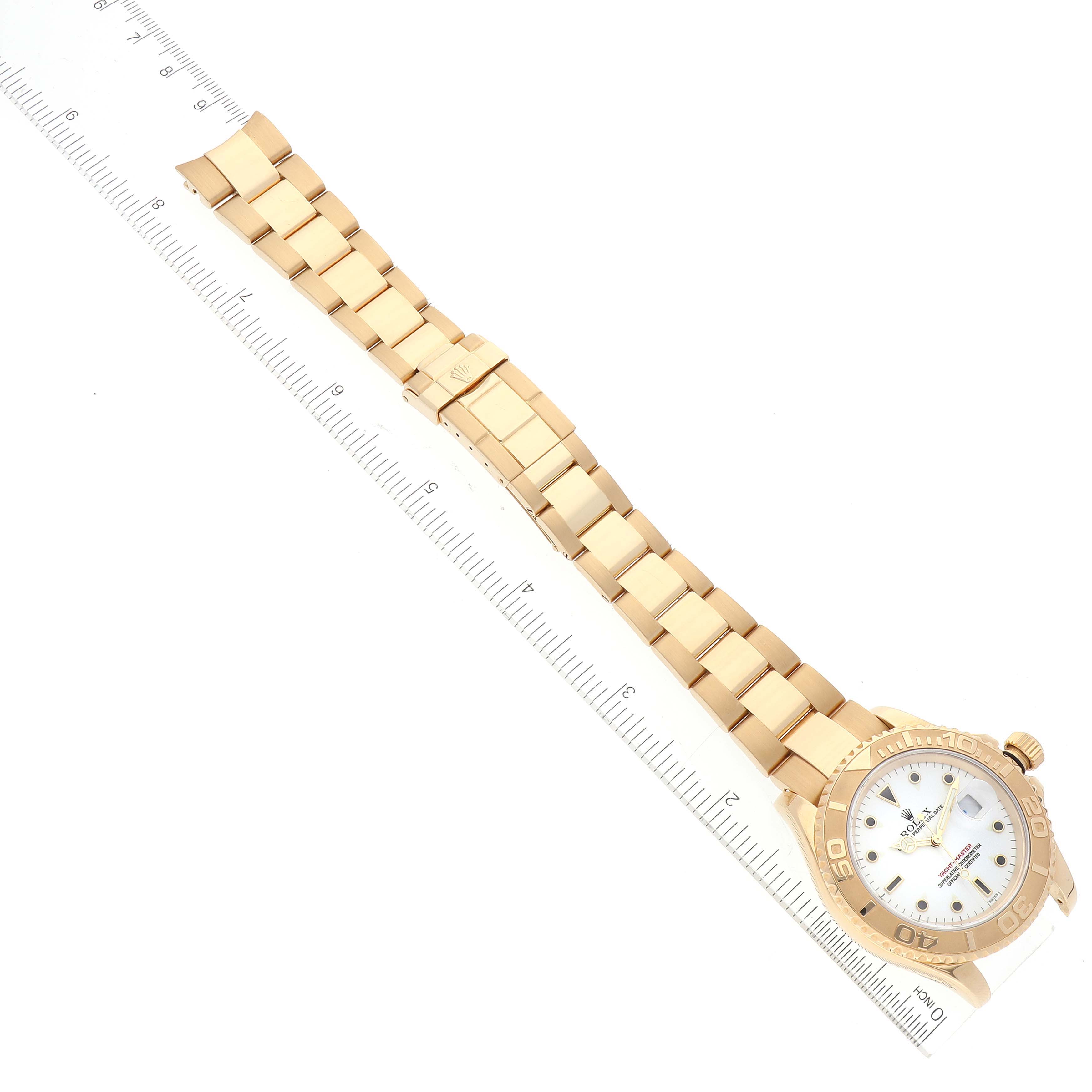 The image shows a top-down view of a Rolex Yacht-Master 16628 Men
s Yellow Gold White Dial 16628 Men
s Yellow Gold White Dial watch, including its face, bezel, and full bracelet, next to a ruler for scale.