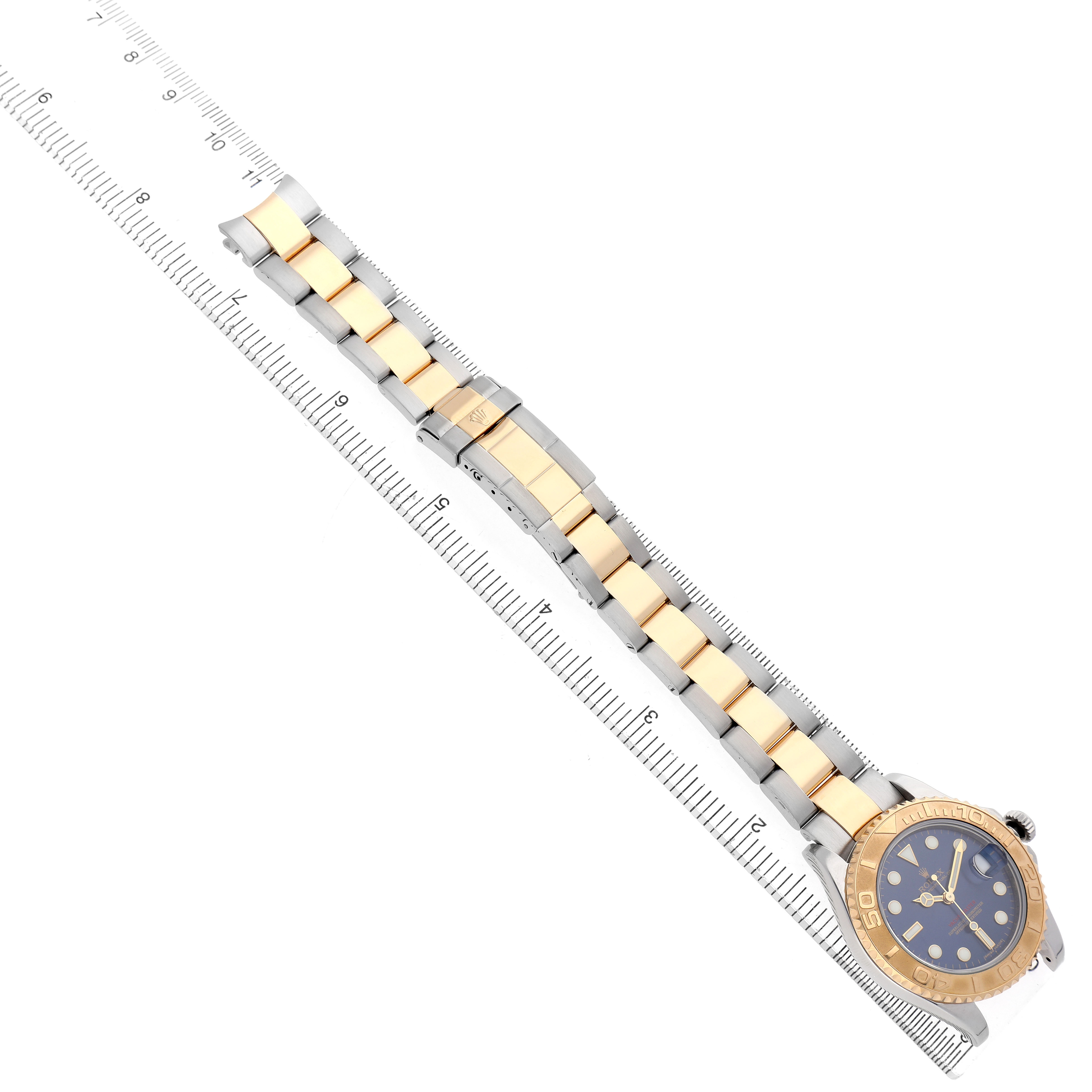 The Rolex Yacht-Master 168623 Men's Steel and Gold (two tone) Blue Dial watch is shown from a top-down angle, highlighting the bracelet, watch face, and bezel beside a ruler.