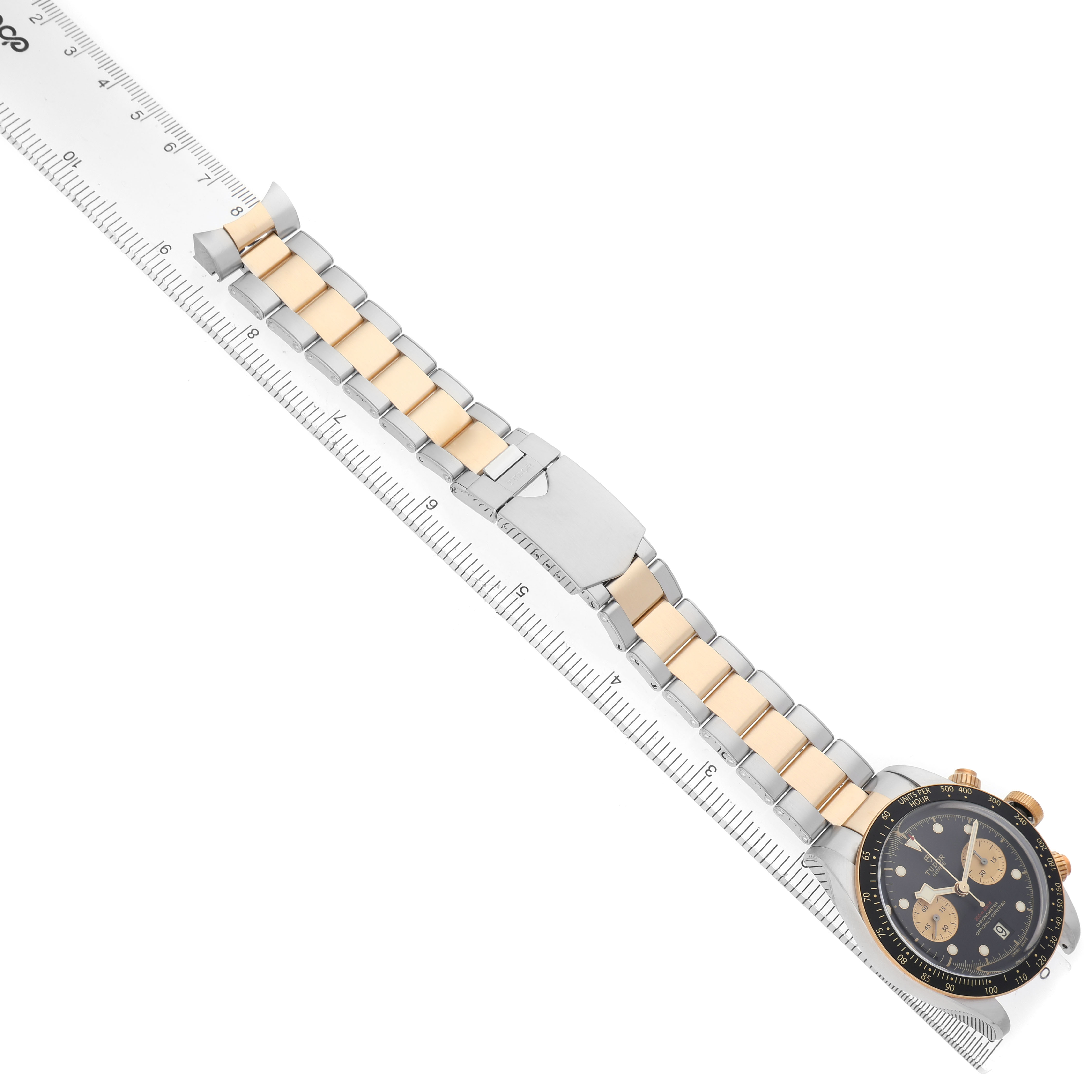 The Tudor Heritage Black Bay 79363N Men's Steel and Gold (two tone) Black Dial watch is shown at an angle, displaying the face, bezel, and part of the two-tone bracelet alongside a ruler.