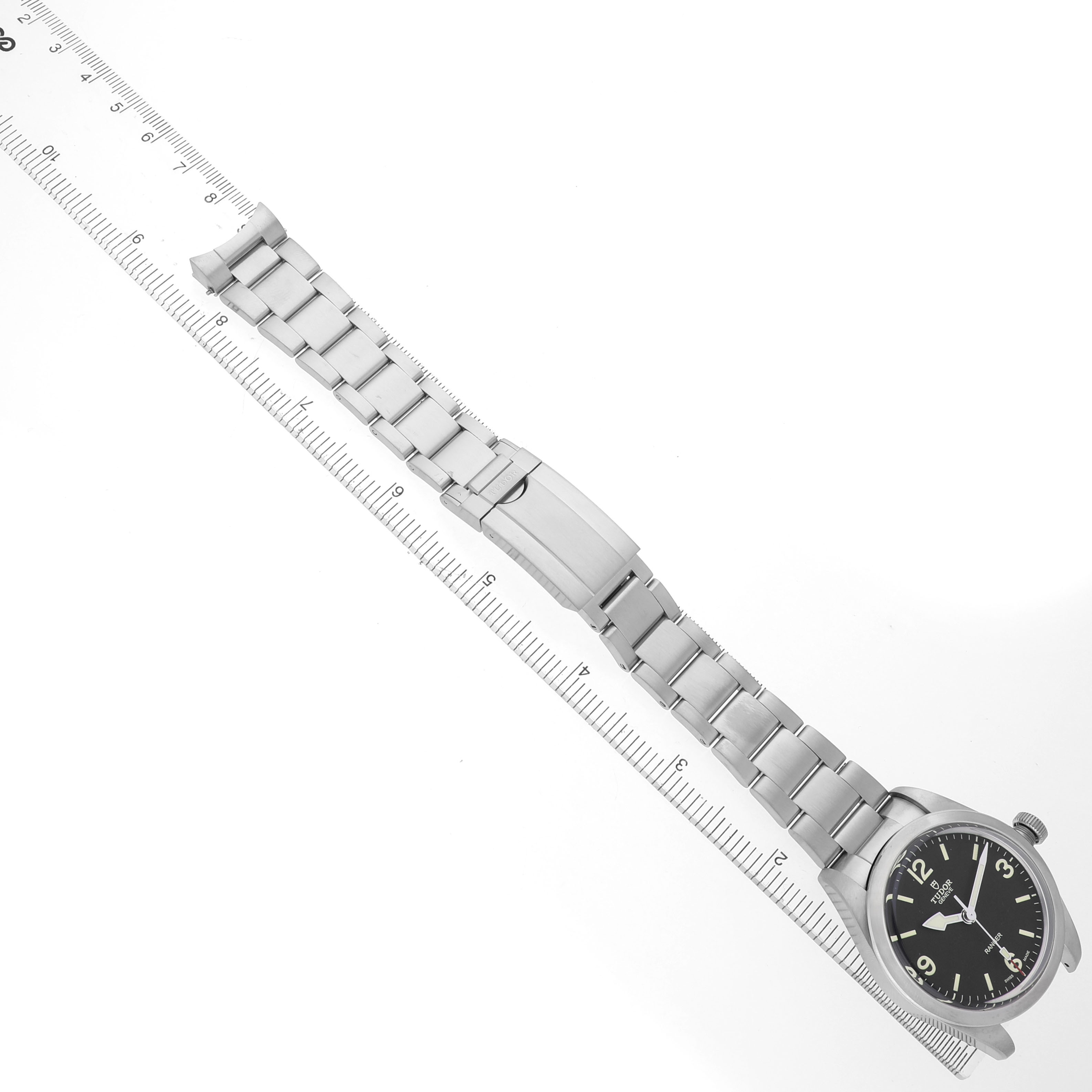 The Tudor Heritage Ranger 79950-0001 Men's Stainless Steel Black Dial watch is shown from an overhead angle alongside a ruler, displaying the full stainless steel bracelet and clasp.
