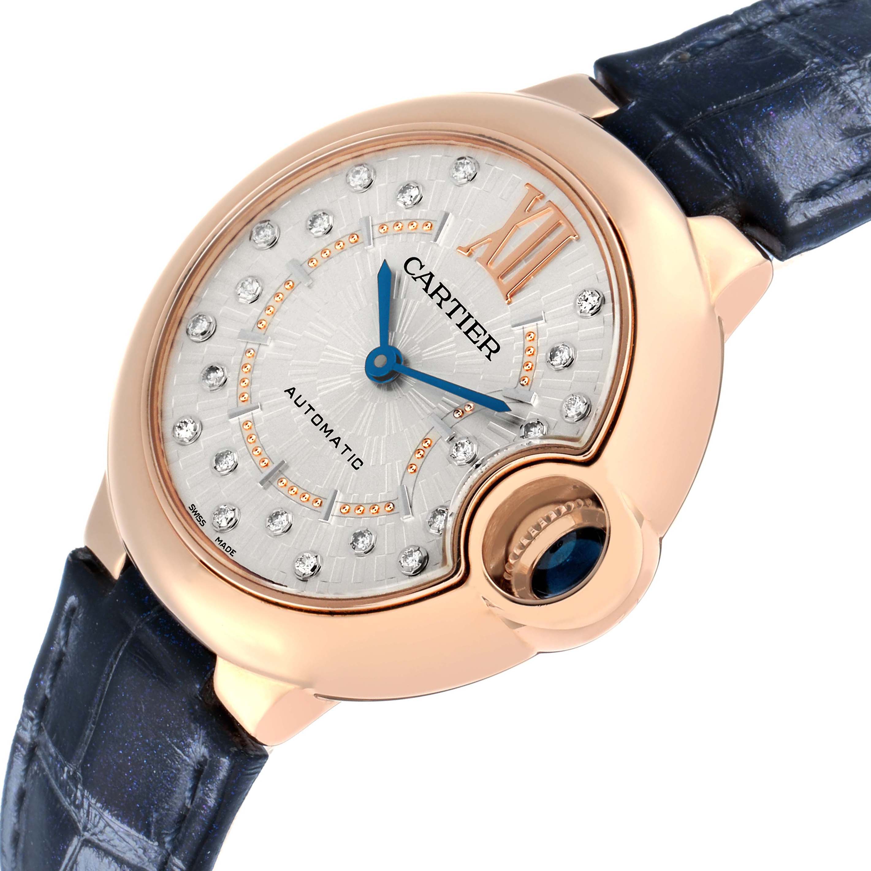 The Cartier Ballon Bleu WGBB0053 Women
s Rose Gold Silver Dial watch is shown at an angle, highlighting its rose gold case, diamond hour markers, blue hands, and navy strap.