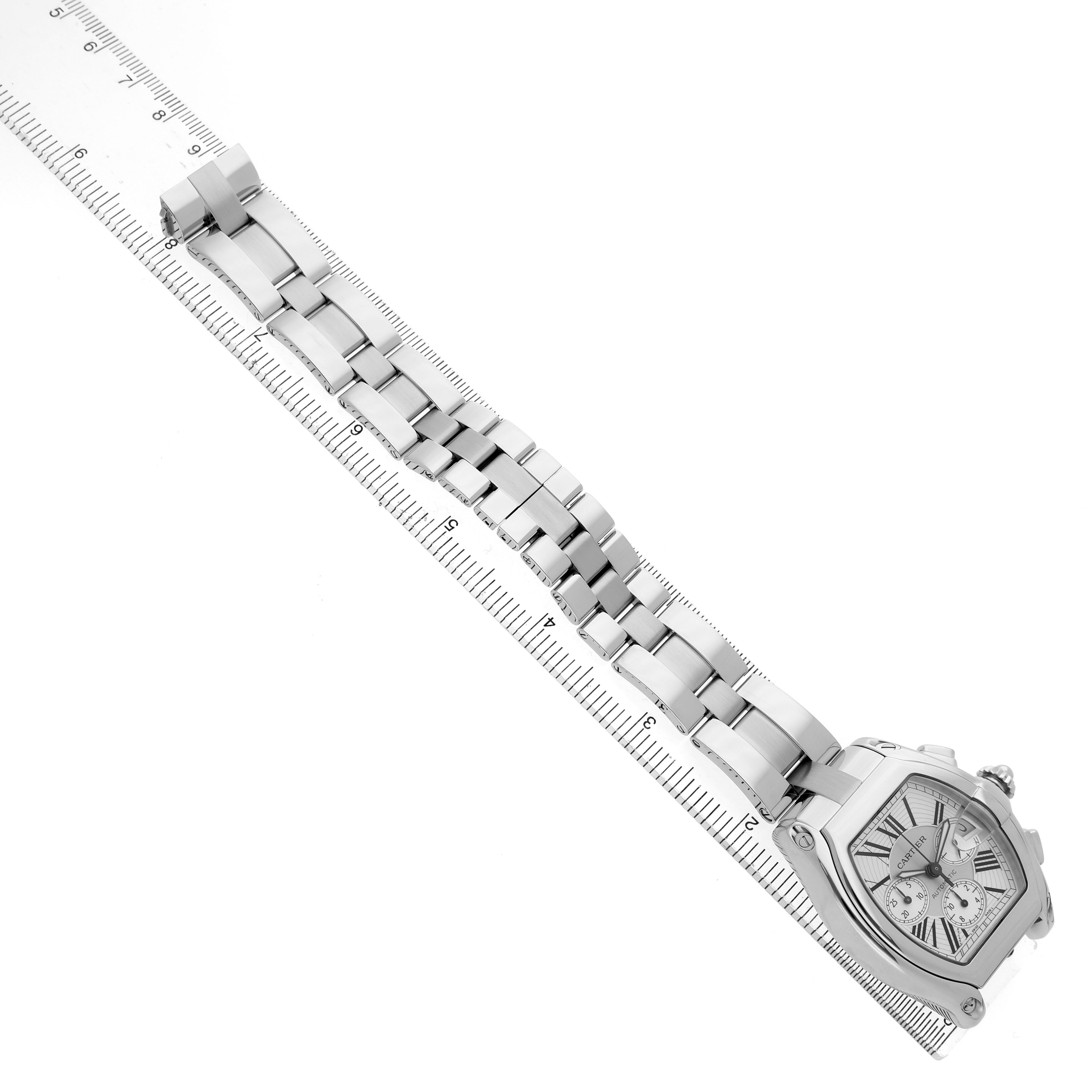 The Cartier Roadster W62019X6 Men's Stainless Steel Silver Dial watch is shown at an angled view, highlighting the face and metal bracelet, set against a ruler.