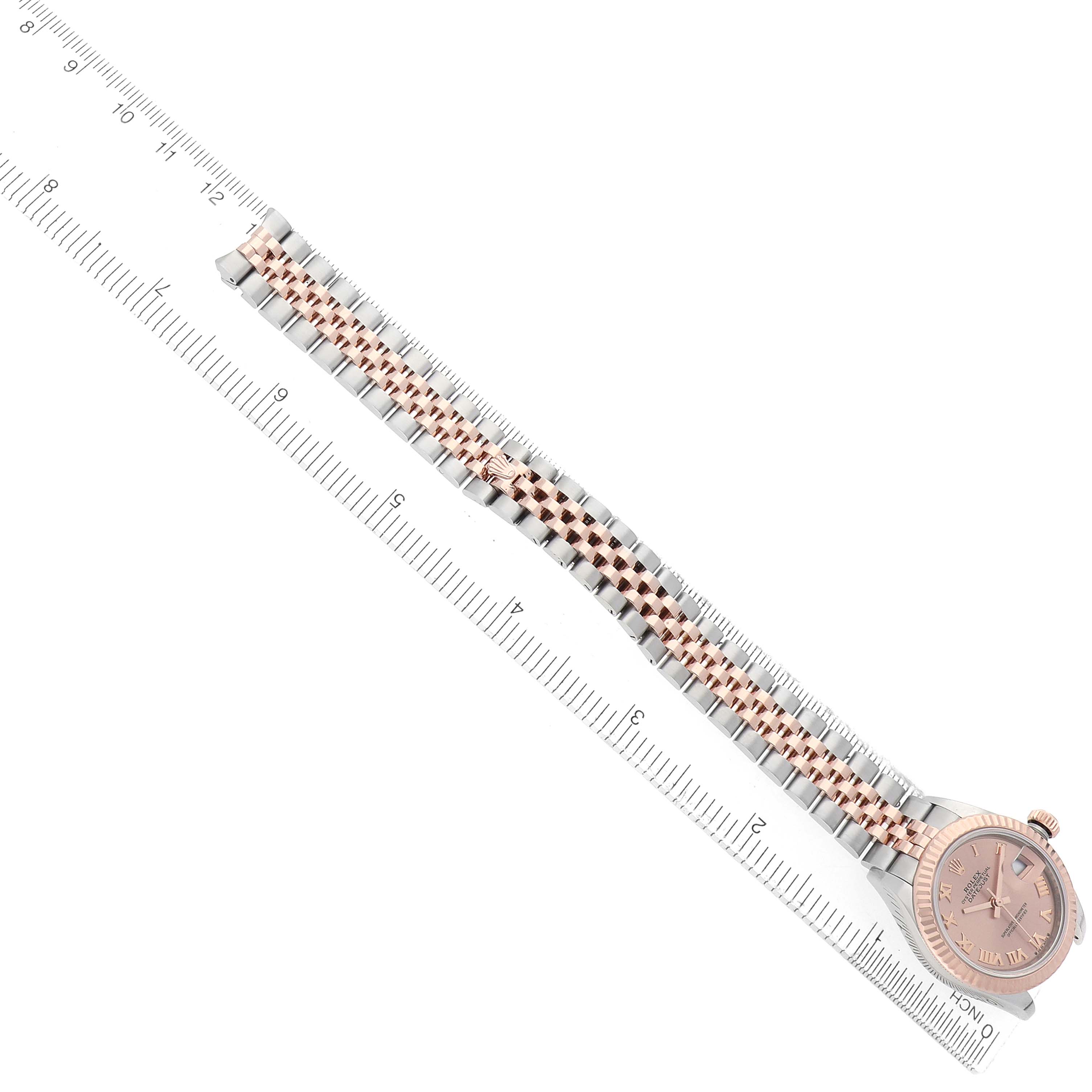 The Rolex Datejust 279171 Women
s Steel and Gold (two tone) Pink Dial watch is shown from a top-down angle, highlighting the face and metal bracelet against a ruler for scale.