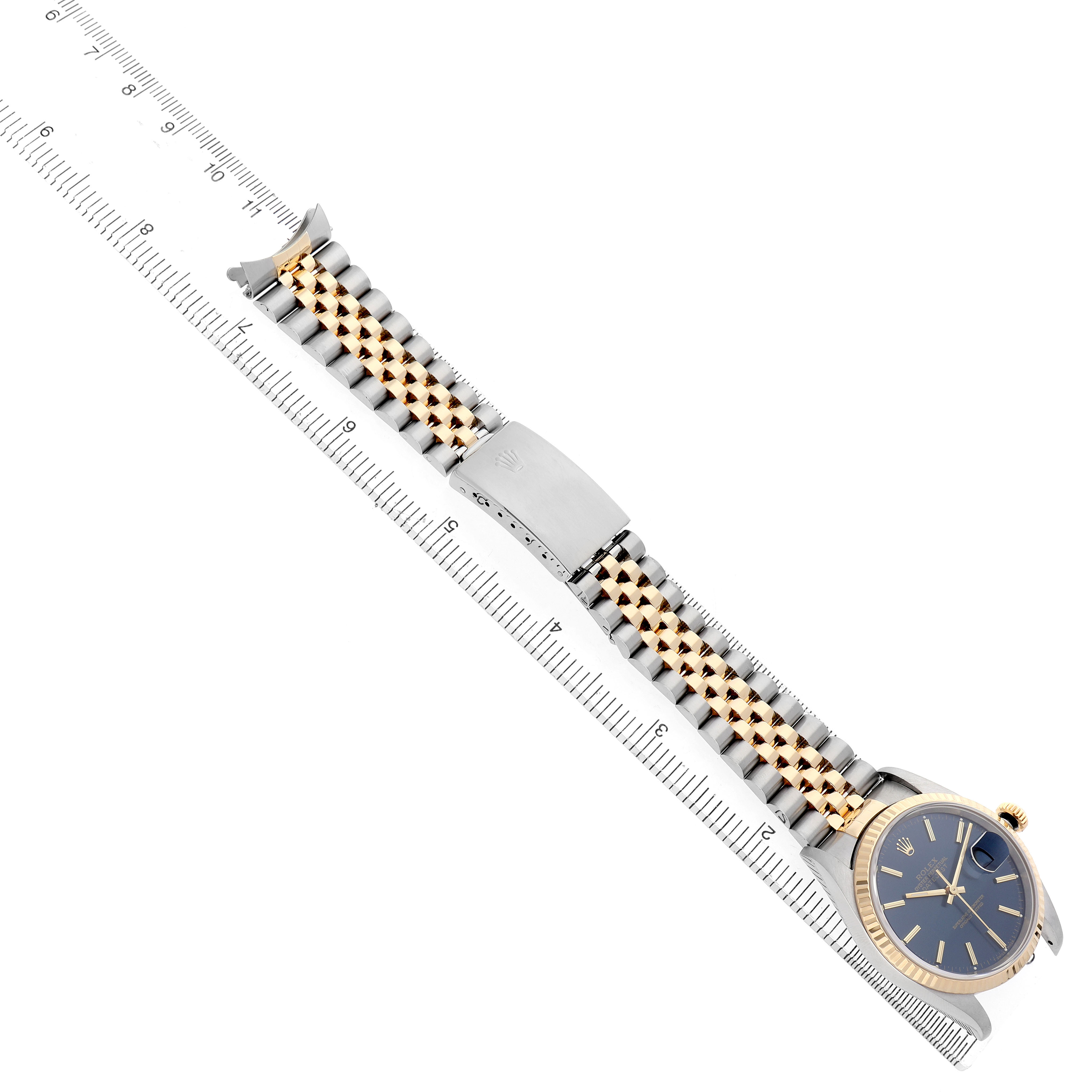 The Rolex Datejust 16233 Men's Steel and Gold (two tone) Blue Dial watch is shown diagonally with the bracelet extended, featuring the bezel, crown, and clasp against a ruler backdrop.