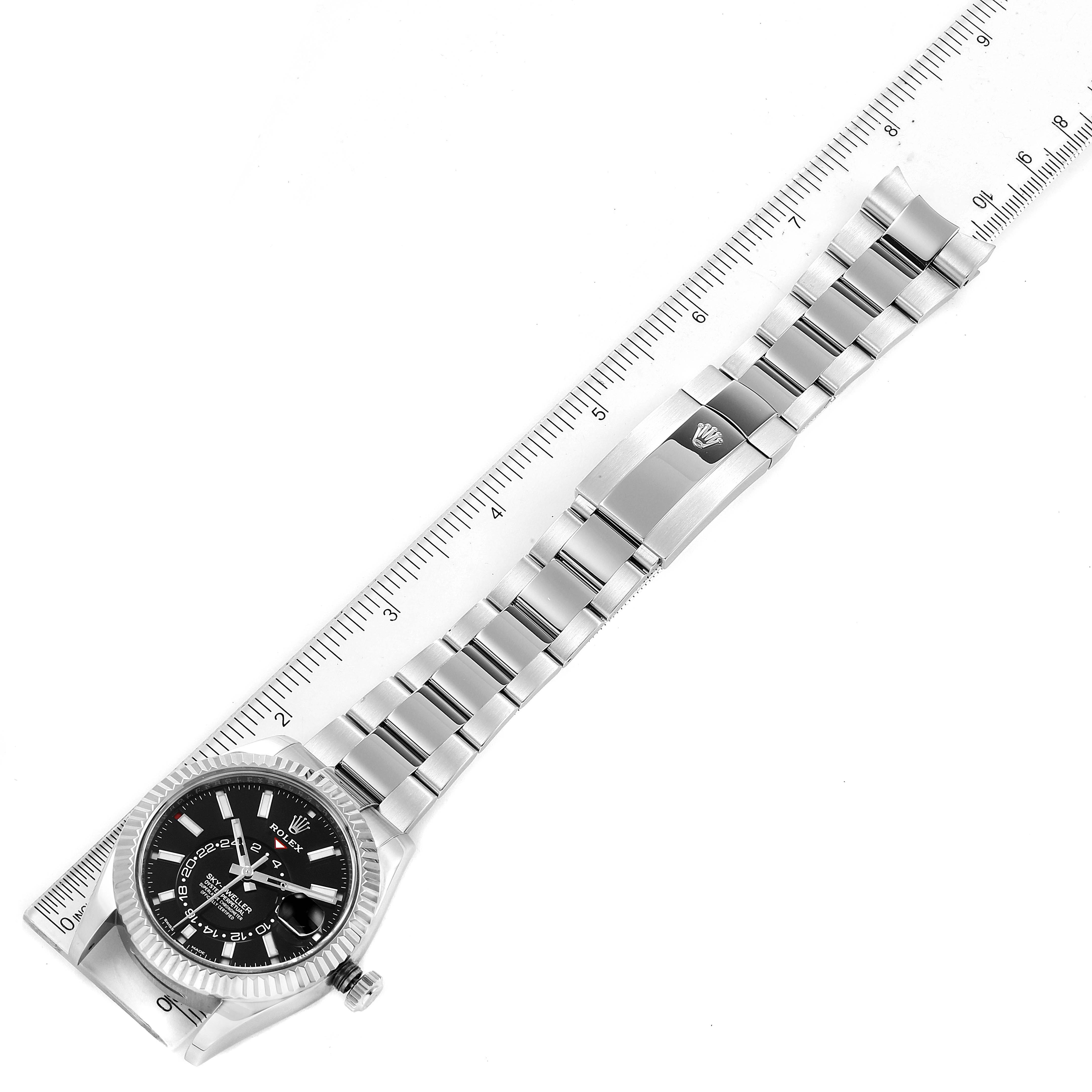 The image shows a top-down view of a Rolex Sky-Dweller 326934 Men's Stainless Steel Black Dial 326934 Men's Stainless Steel Black Dial watch, including the dial, bezel, case, bracelet, and clasp, next to a ruler.