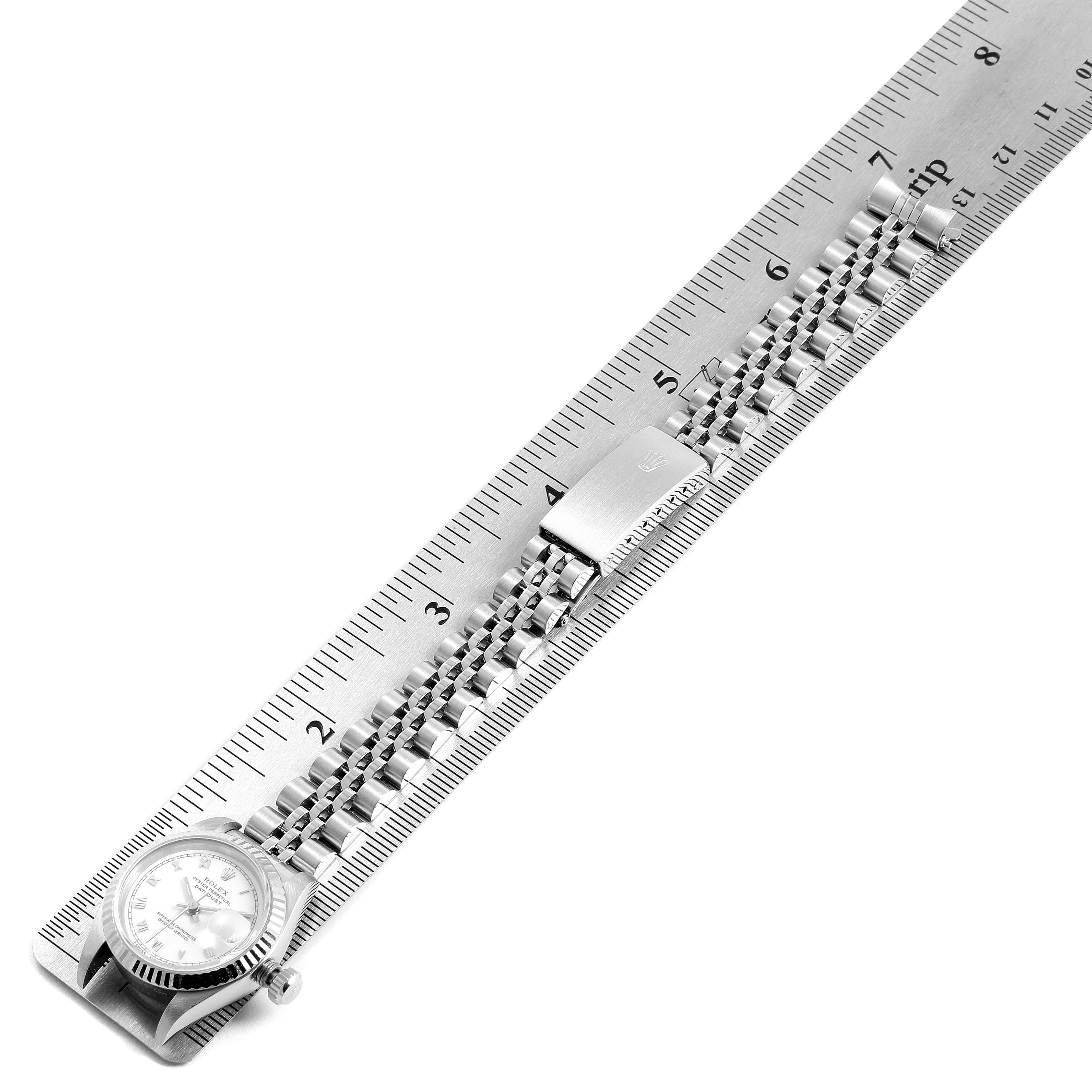This image shows the Rolex Datejust 69174 Women's Stainless Steel White Dial 69174 Women's Stainless Steel White Dial watch laid flat on a metal ruler, showcasing the face, bezel, and bracelet from a top-down angle.