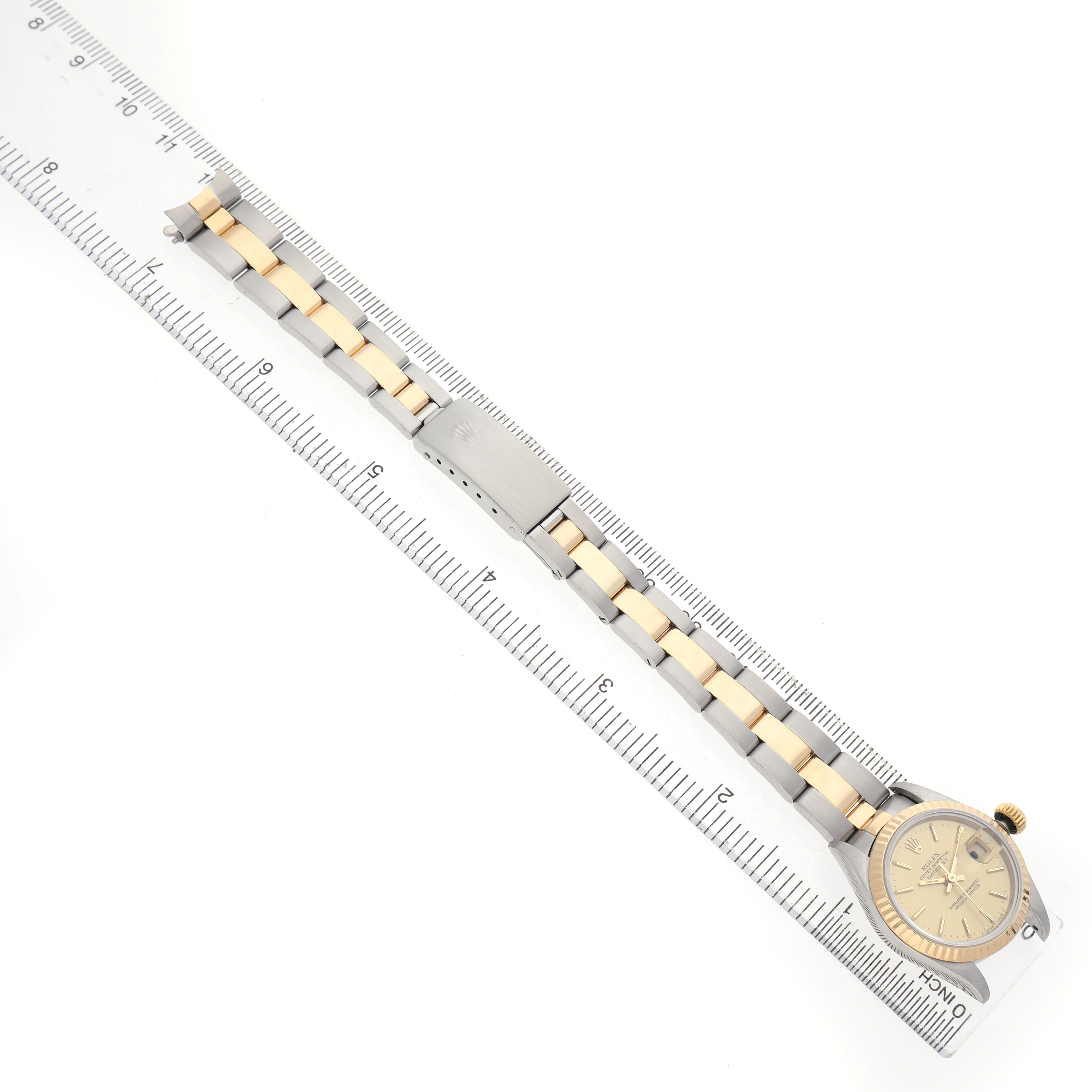 The Rolex Datejust 69173 Women's Steel and Gold (two tone) Champagne Dial watch is shown from an overhead angle, displaying the full bracelet, clasp, and face next to a ruler.