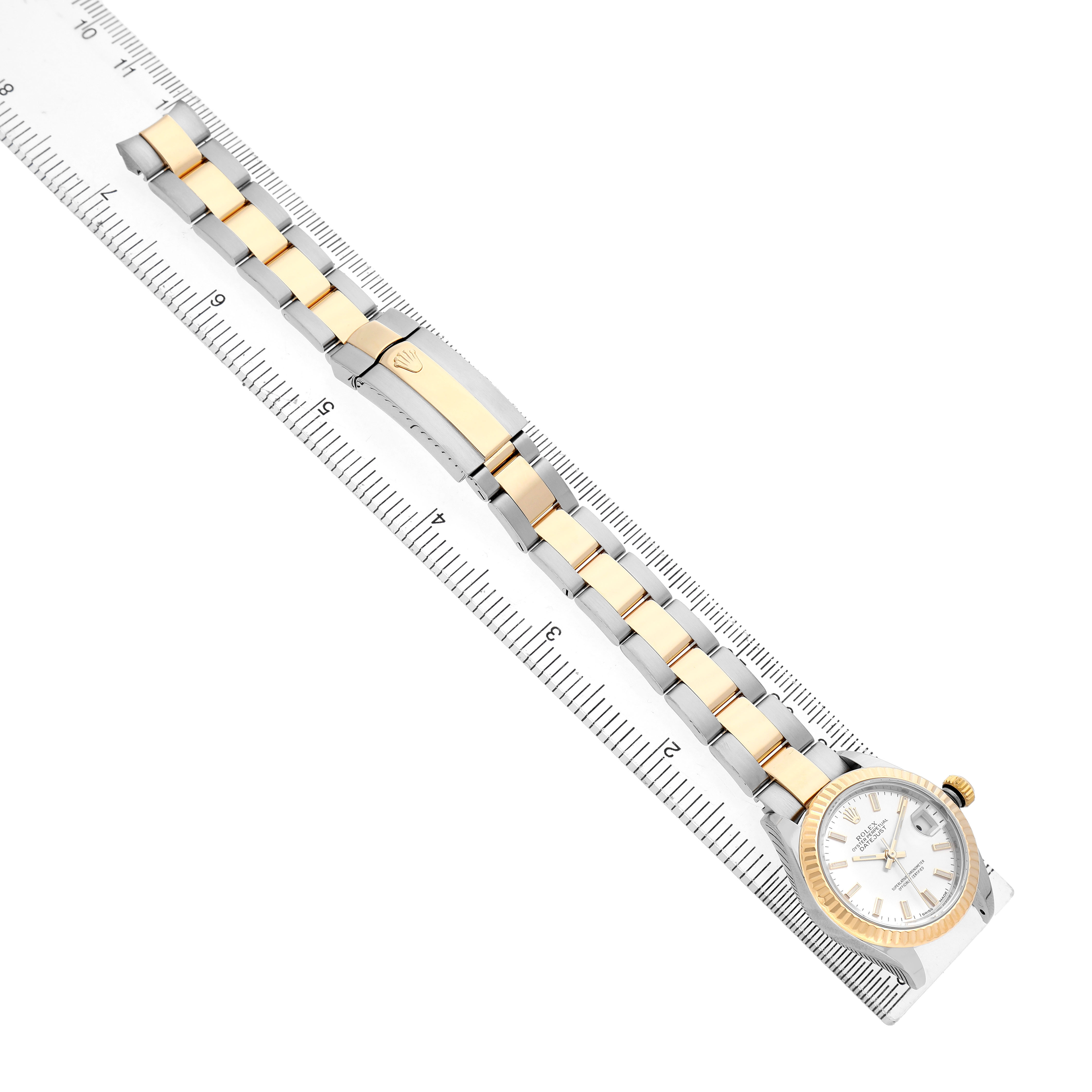 The Rolex Datejust 279173 Women's Steel and Gold (two tone) Silver Dial watch is shown from the top, displaying its full bracelet and clasp next to a ruler for scale.