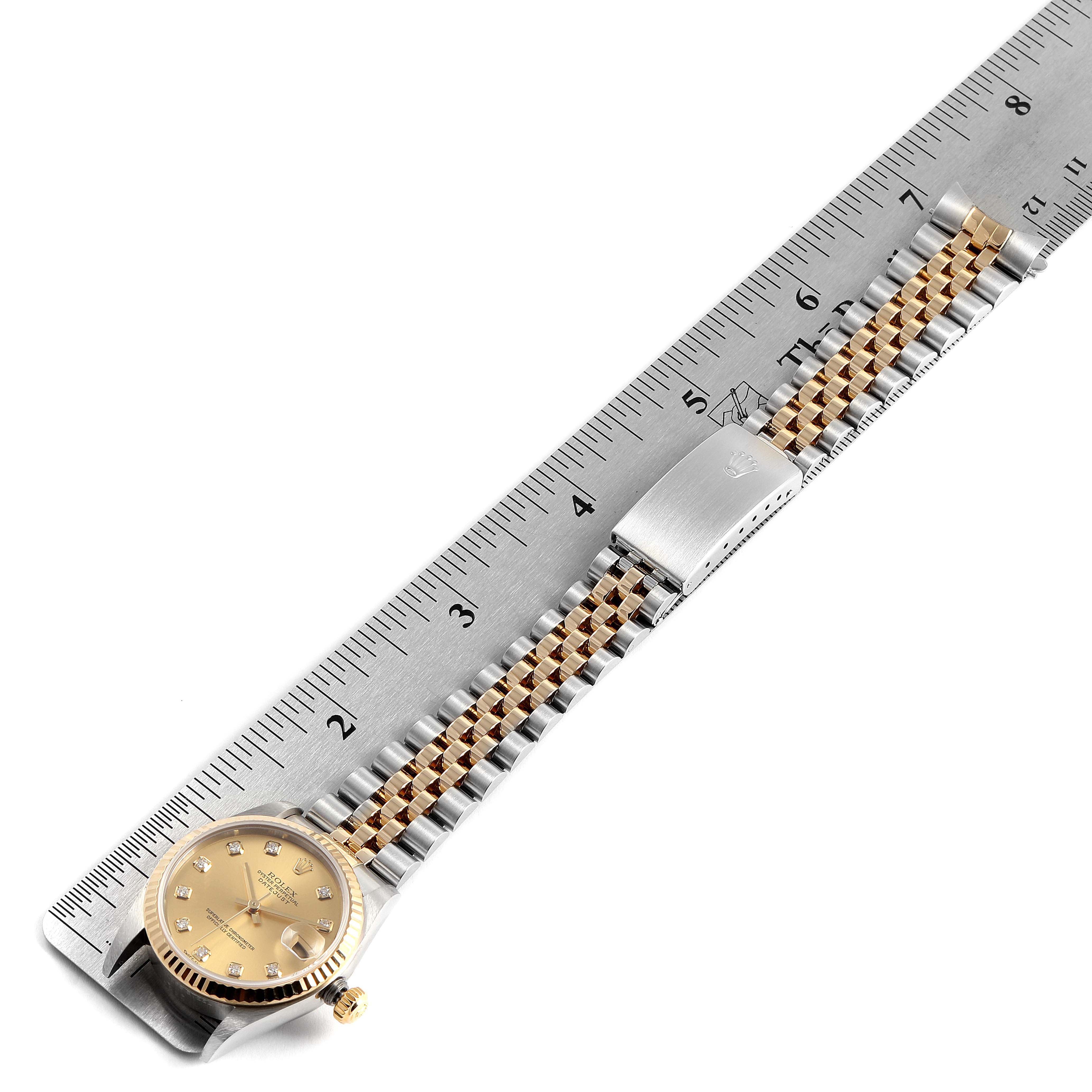 The image shows a Rolex Mid-Size 78273 Women
s Steel and Gold (two tone) Champagne Dial 78273 Women
s Steel and Gold (two tone) Champagne Dial model watch placed alongside a ruler, featuring its face and two-tone metal bracelet.