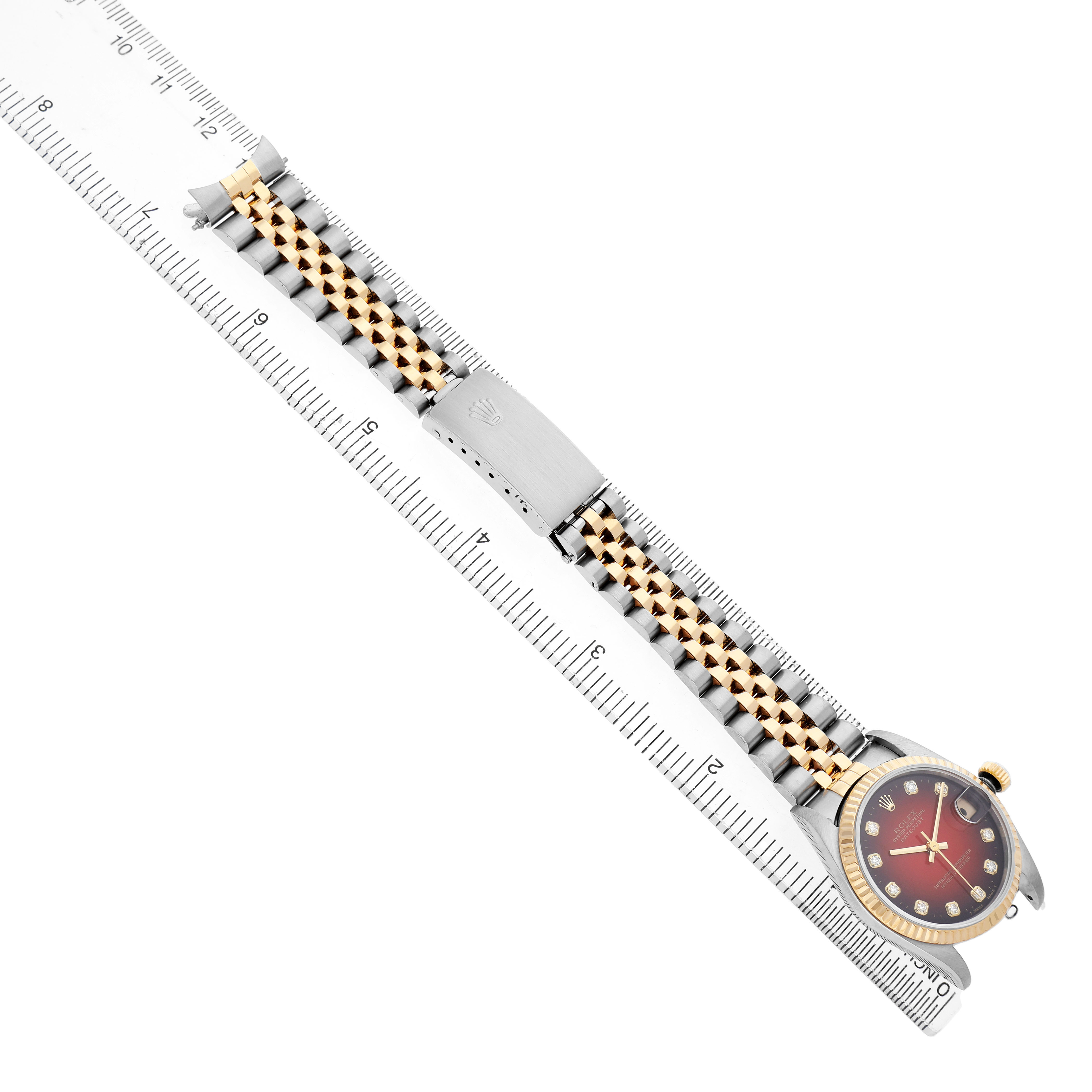 The Rolex Datejust 78273 Women's Steel and Gold (two tone) Red Dial watch is shown from a top-down angle, highlighting the bracelet, case, bezel, and clasp alongside a ruler.